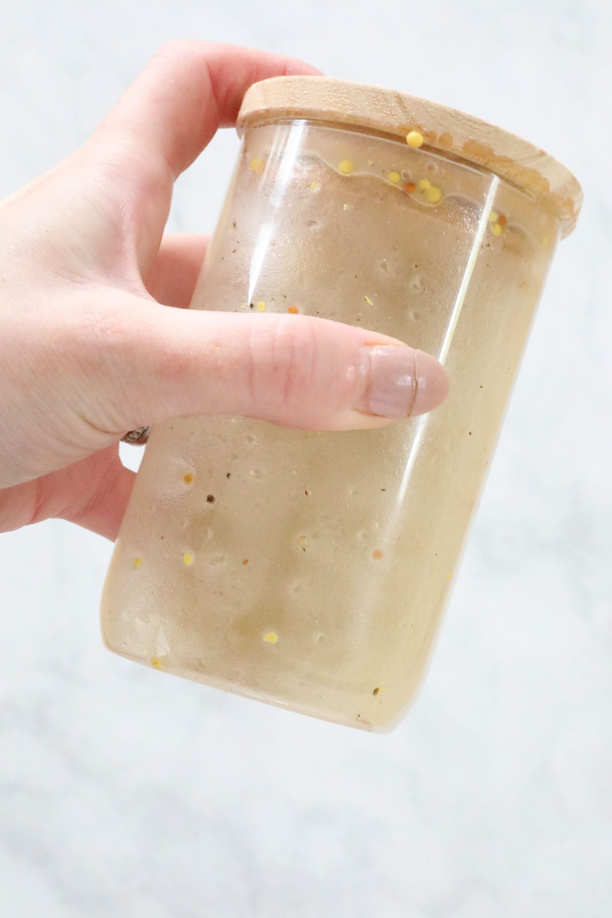 A hand holding the salad ingredients being shaken together in a jar.