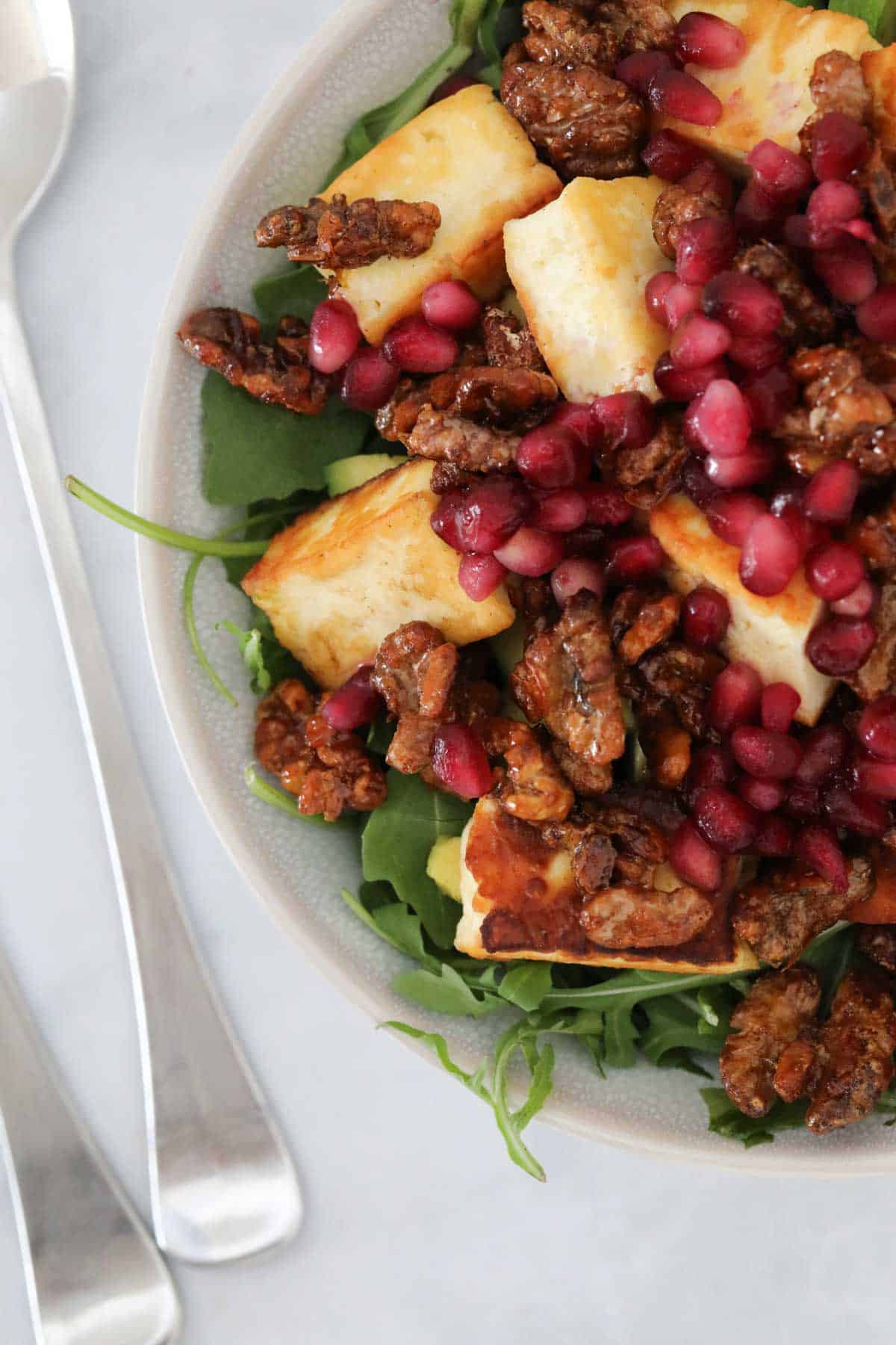 A close up of a serving of halloumi and pomegranate salad topped with walnuts.