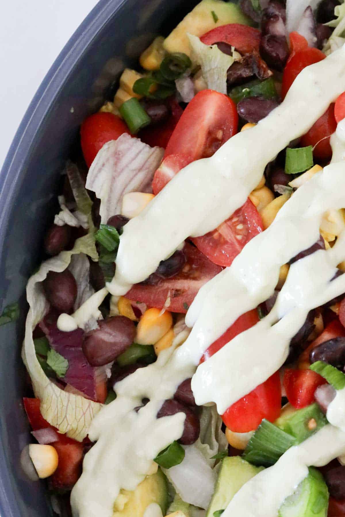 Lime and avocado dressing poured over a bowl of fresh salad ingredients.