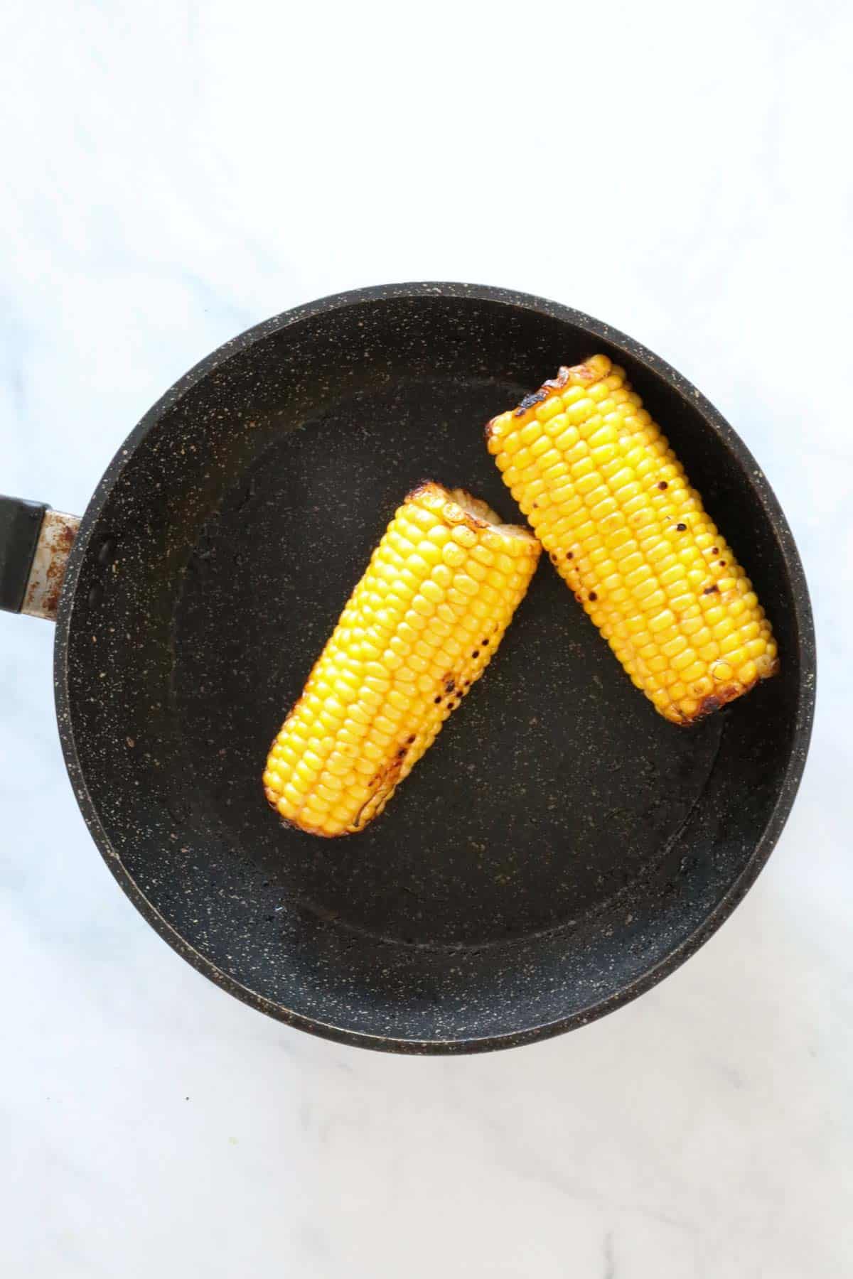 Two corn cobs being charred in a frying pan.