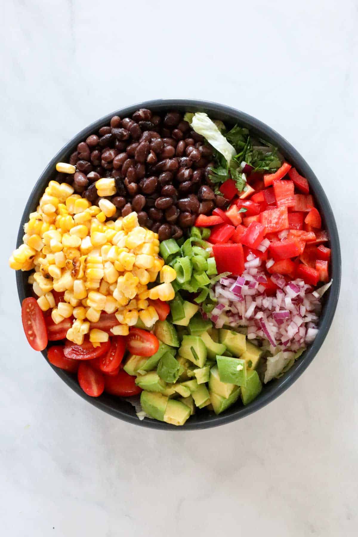 All the chopped salad ingredients in the bowl placed on top of the lettuce.