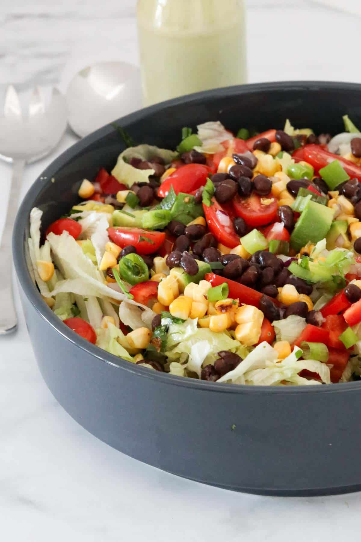 A bowl of Mexican chopped salad with a jar of creamy avocado dressing just visible behind the bowl.