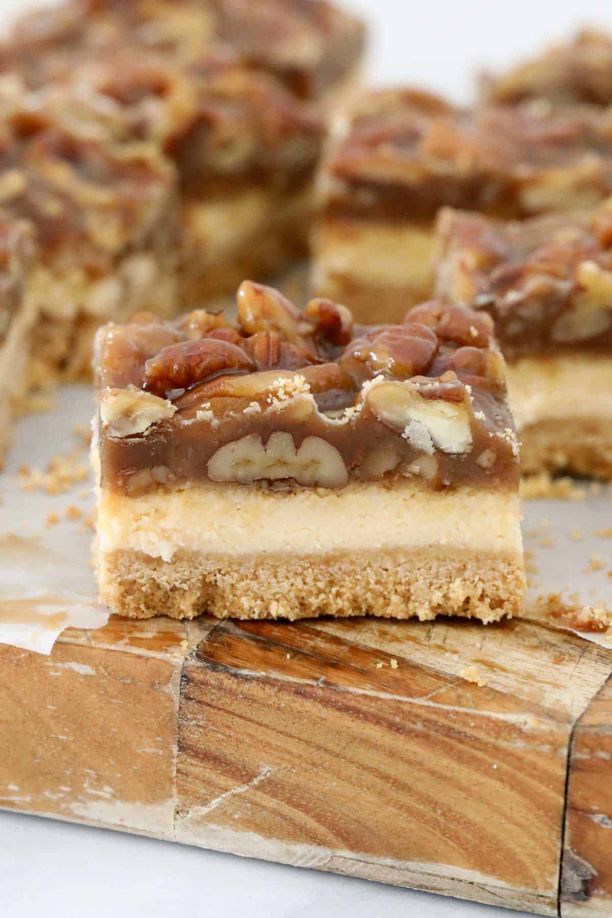 A side view of a bar of the sliced pecan pie cheesecake on a wooden board.