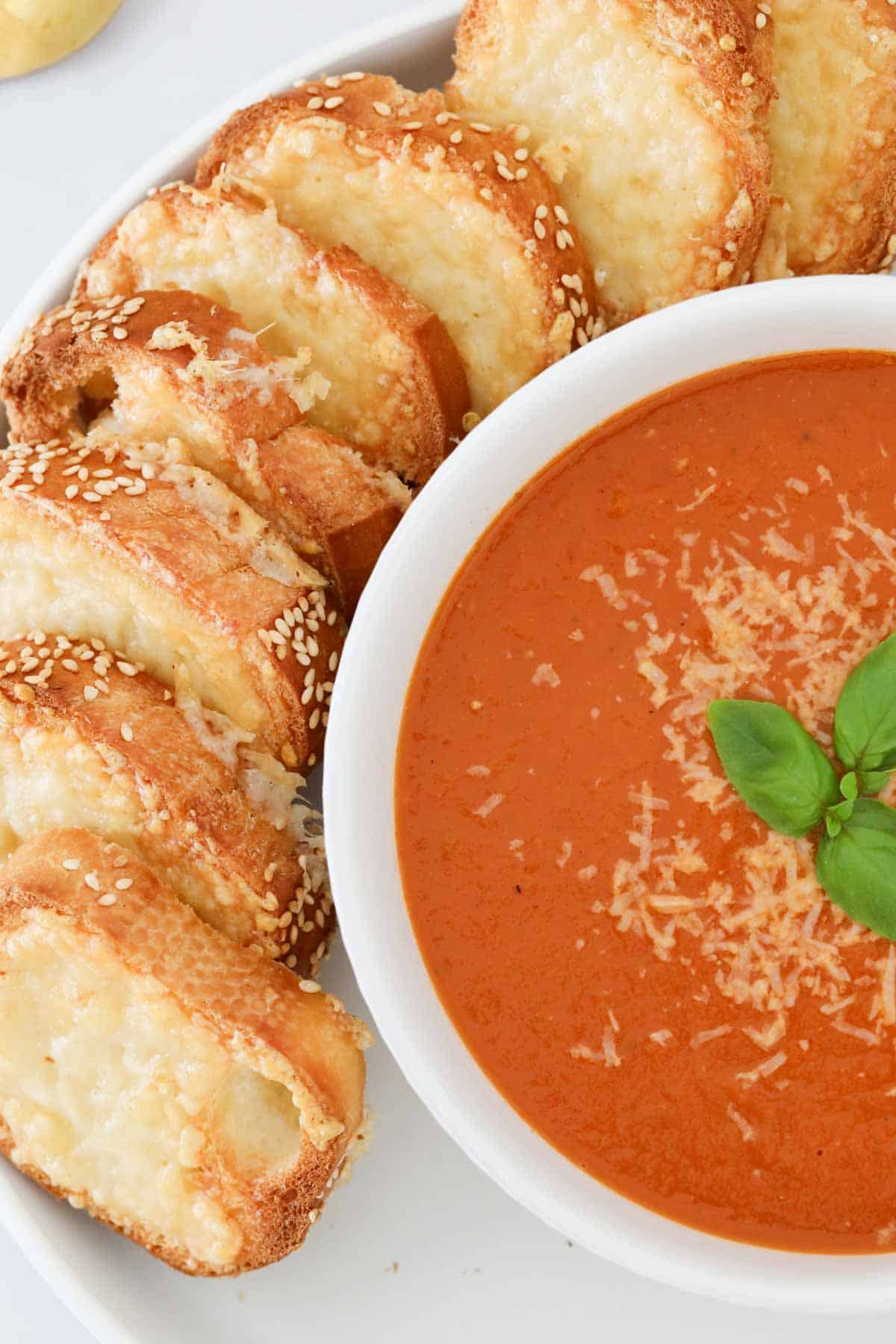 A bowl of soup served sprinkled with parmesan and cheese toasties on the side.