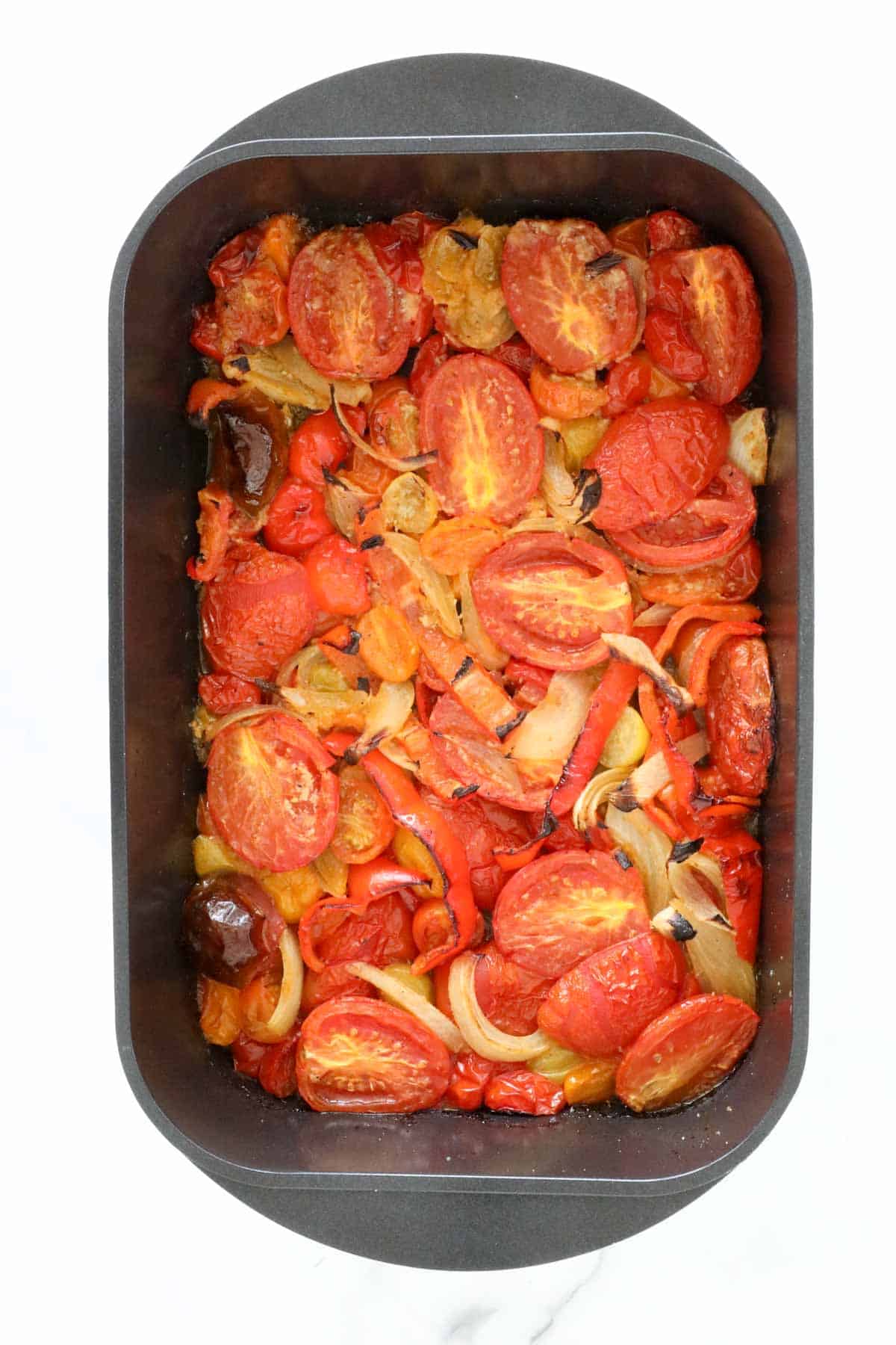 The roasted tomatoes and peppers in the baking dish.