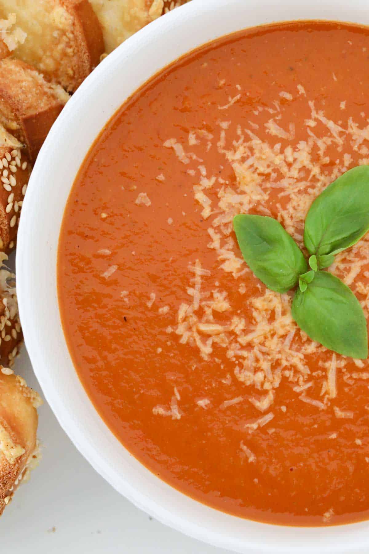 A white bowl filled with roasted tomato soup, sprinkled with parmesan cheese and toped with fresh basil leaves.