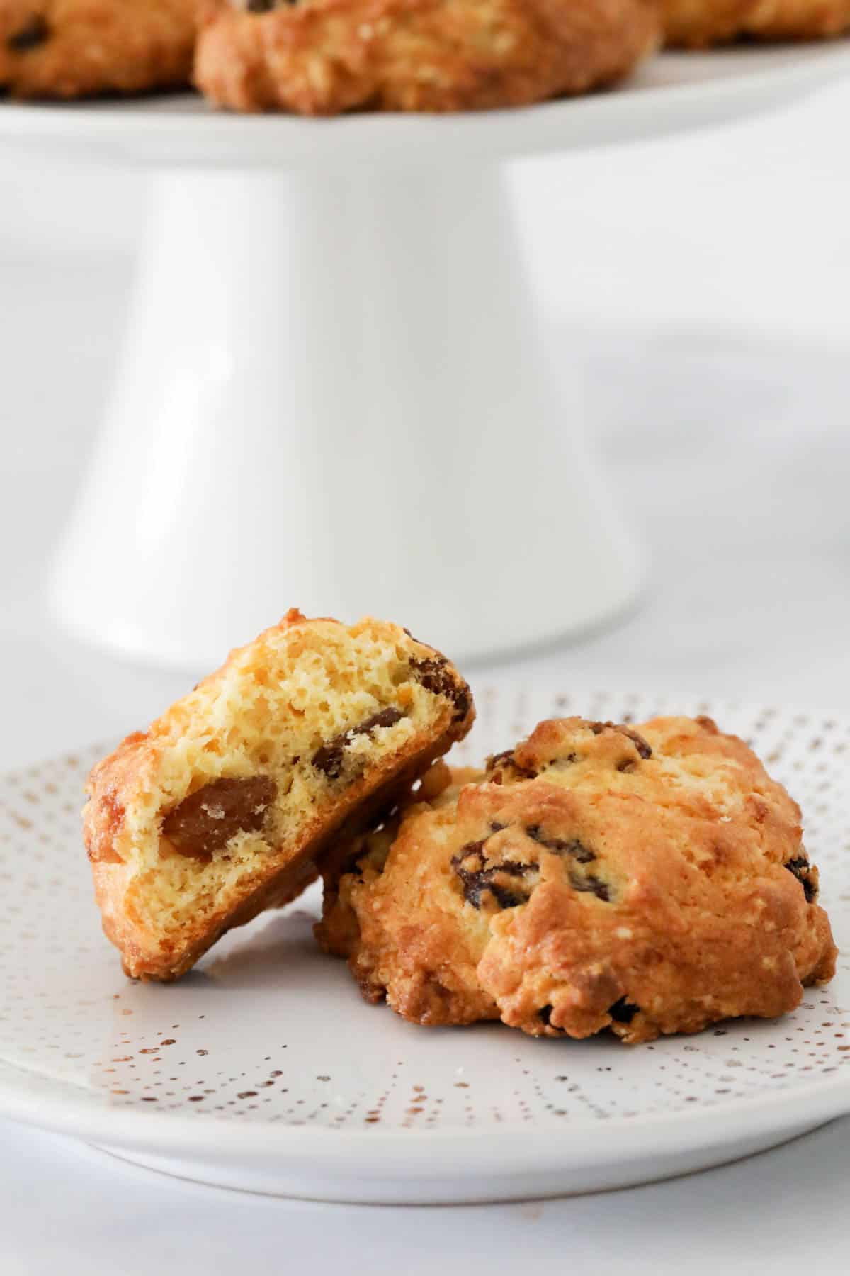 Two rock cakes on a white plate, the other rock cakes on a white cake stand behind.