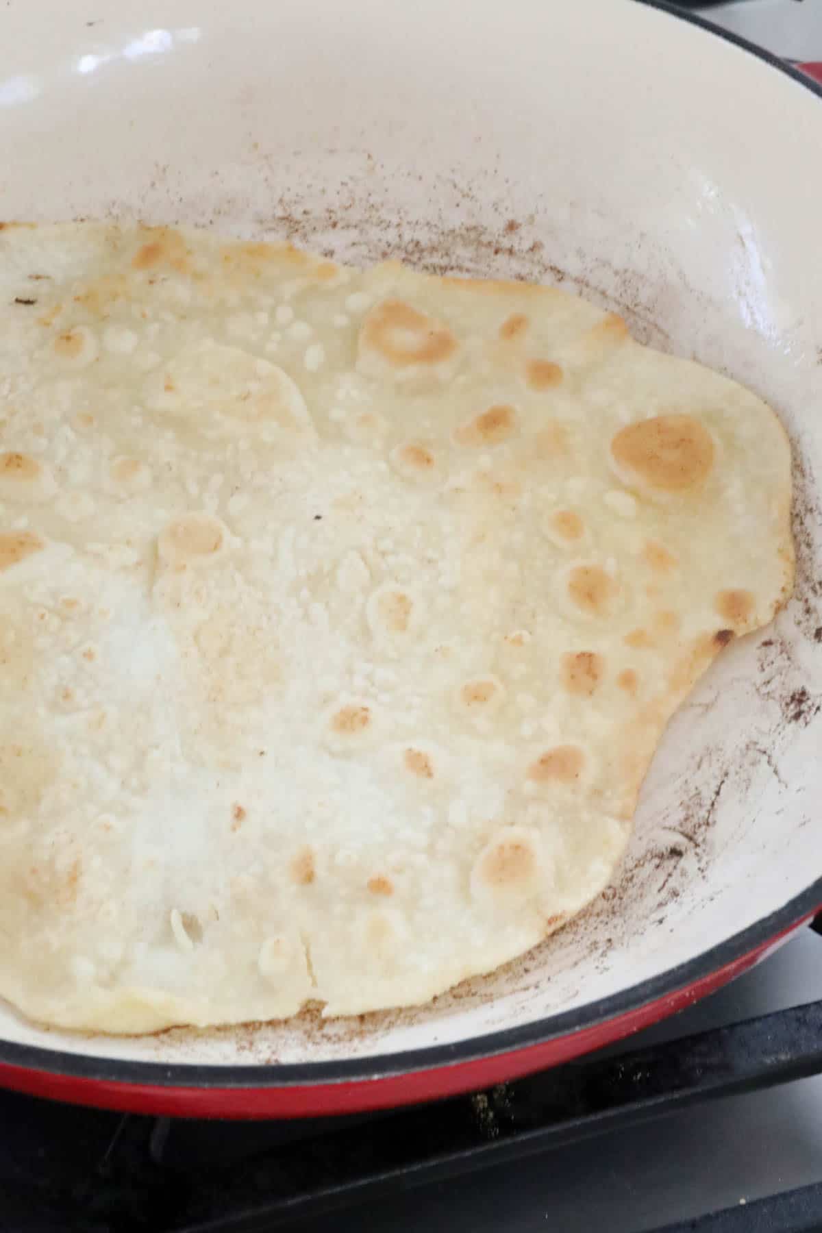 A cooked roti bread in a dry frying pan.