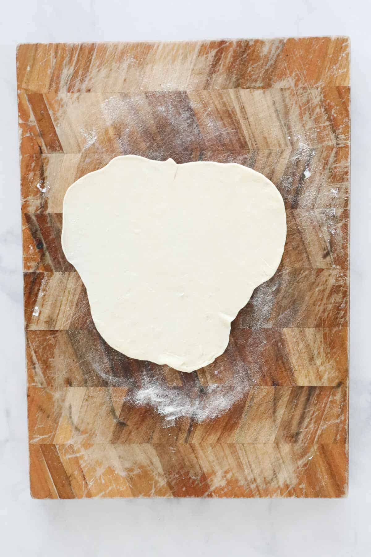 A portion of dough rolled out very thinly on wooden board.