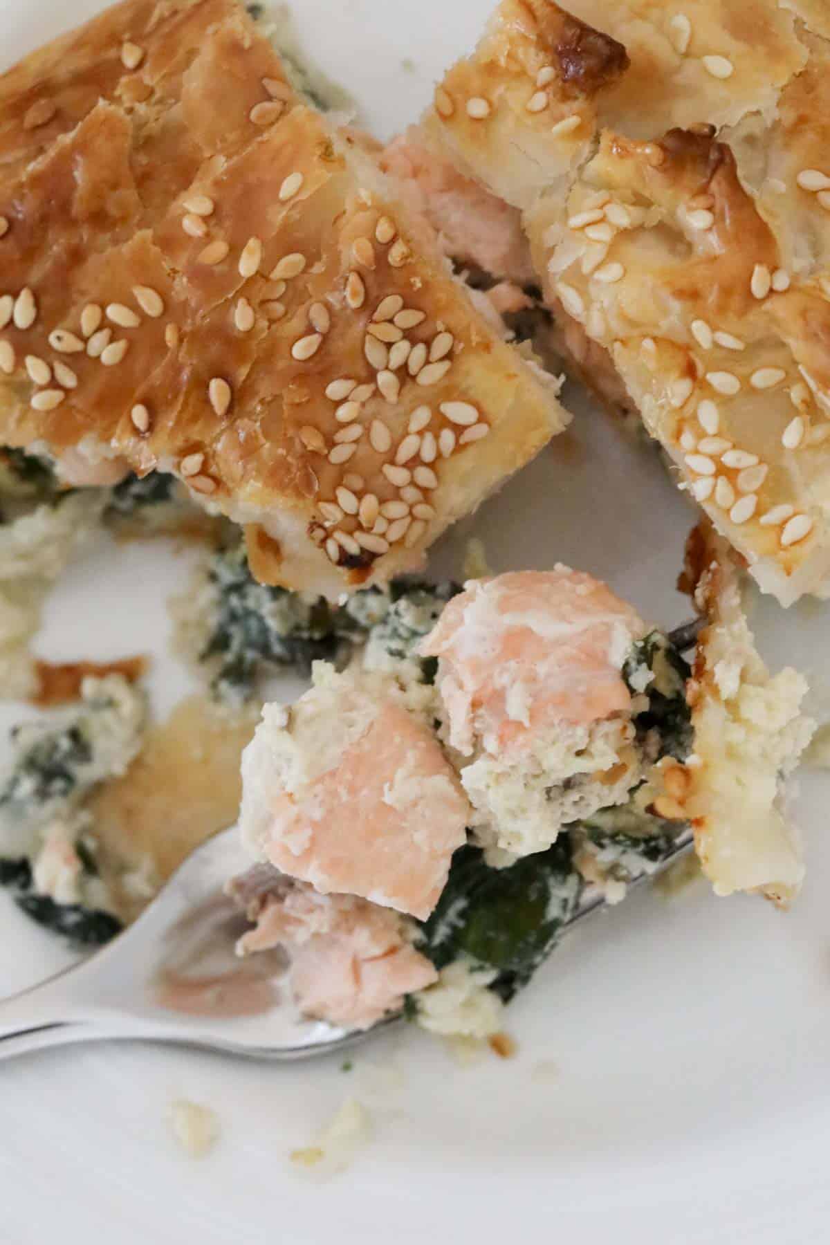 A slice of salmon pie with a fork holding chunks of cooked salmon.