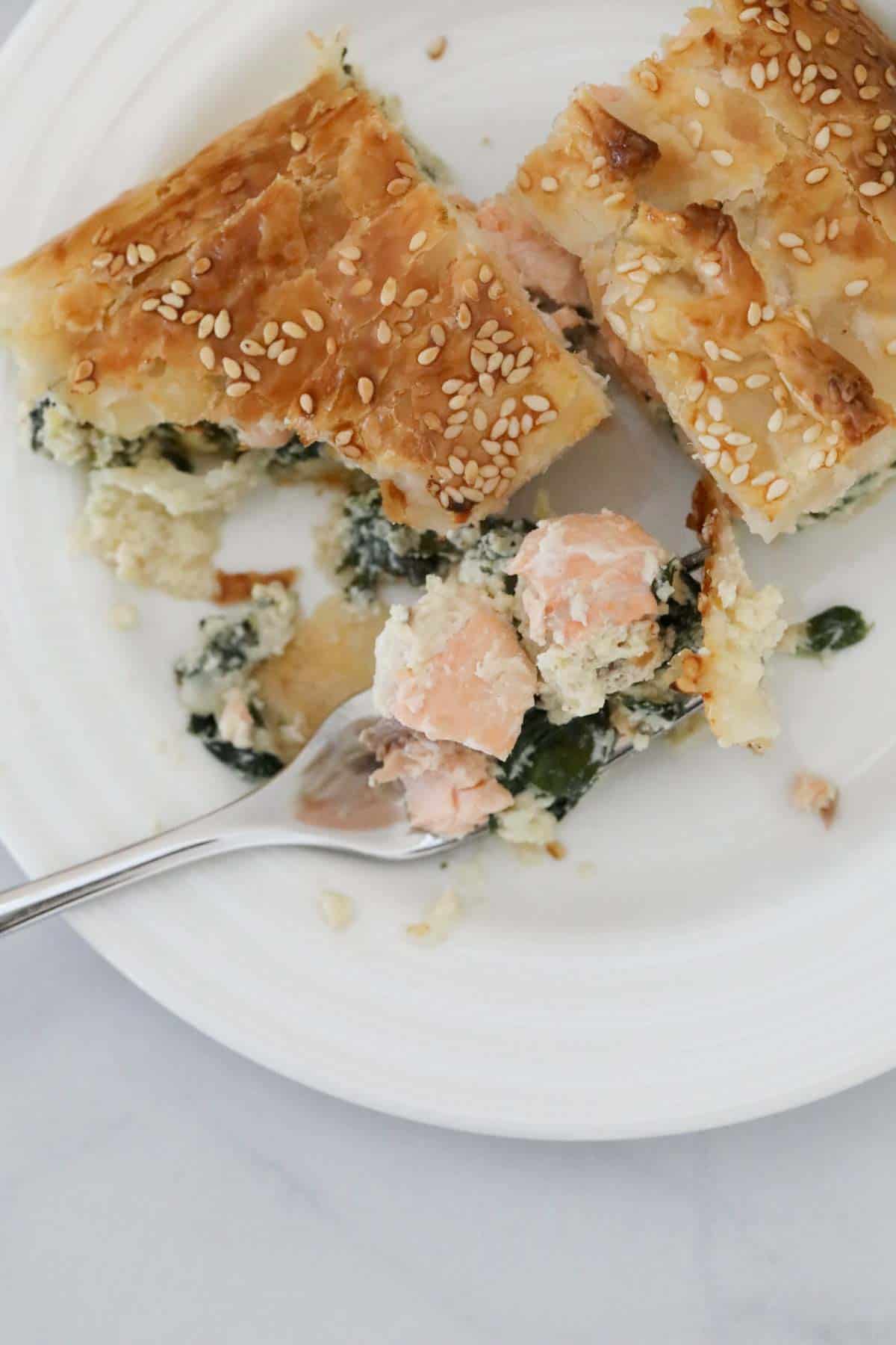 chunks of salmon and spinach on a fork, next to a slice of pie.