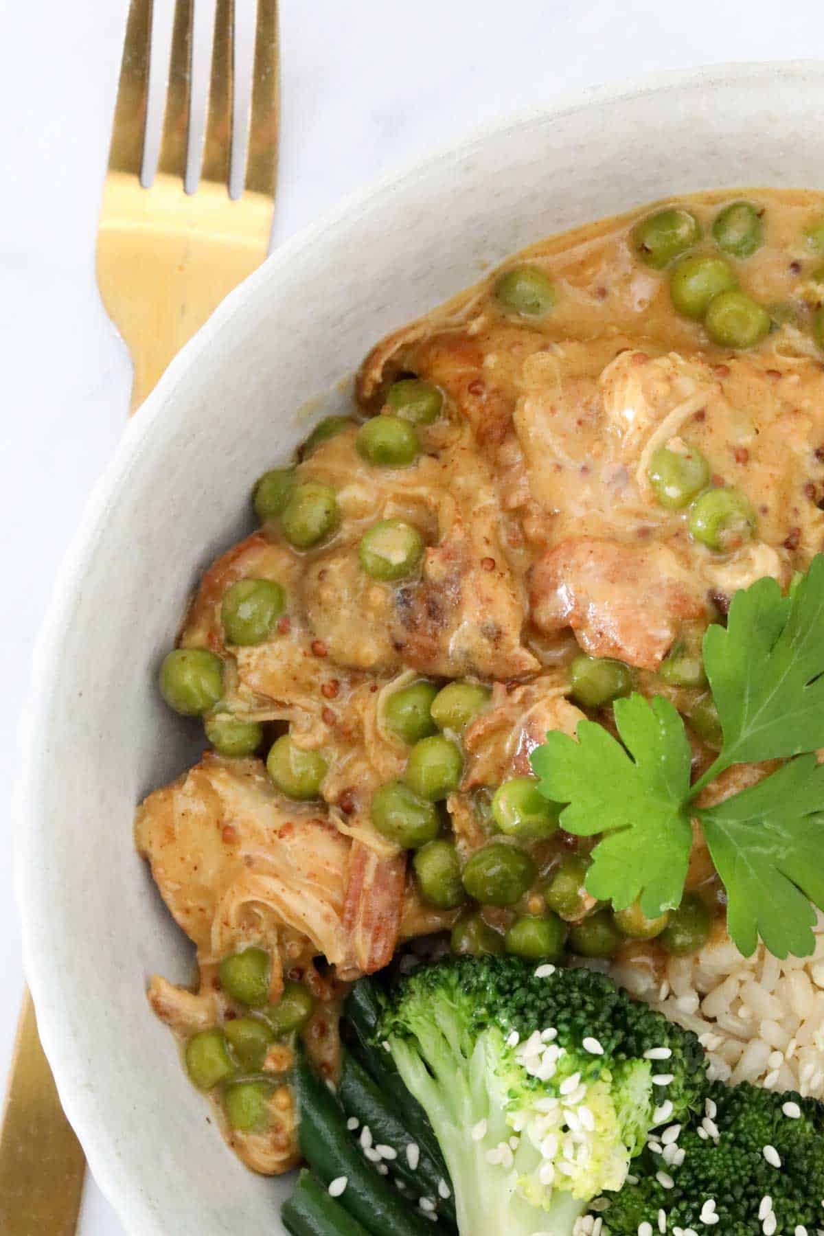 A white serving dish filled with chicken and peas in a creamy mustard sauce.