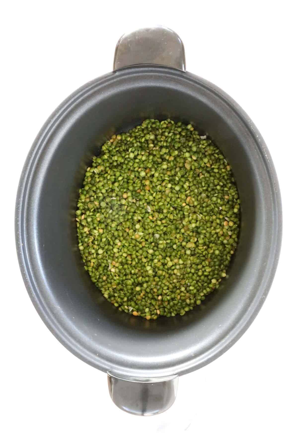 Rinsed green split peas in the bottom of a slow cooker.