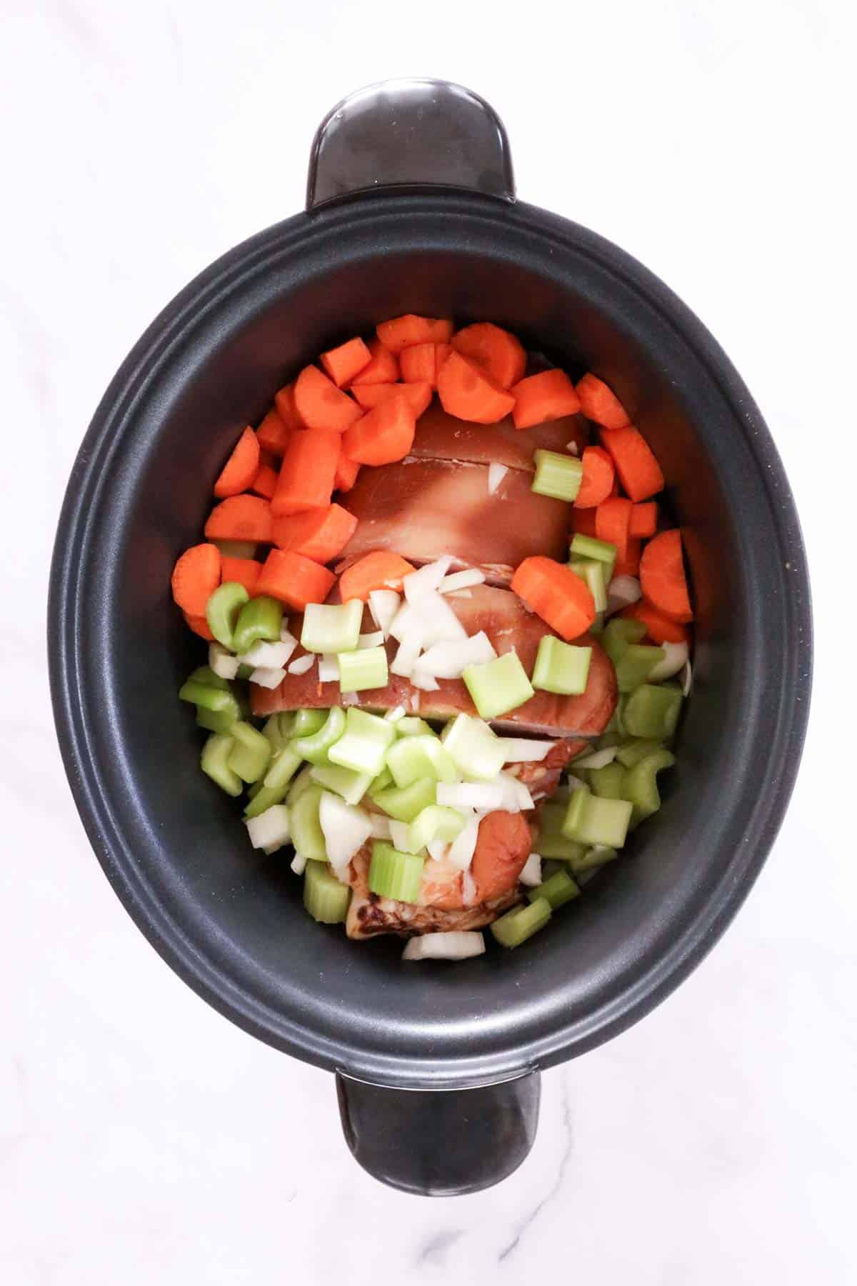 Chopped carrots, celery and onion placed on top of the ham hock in the slow cooker bowl.