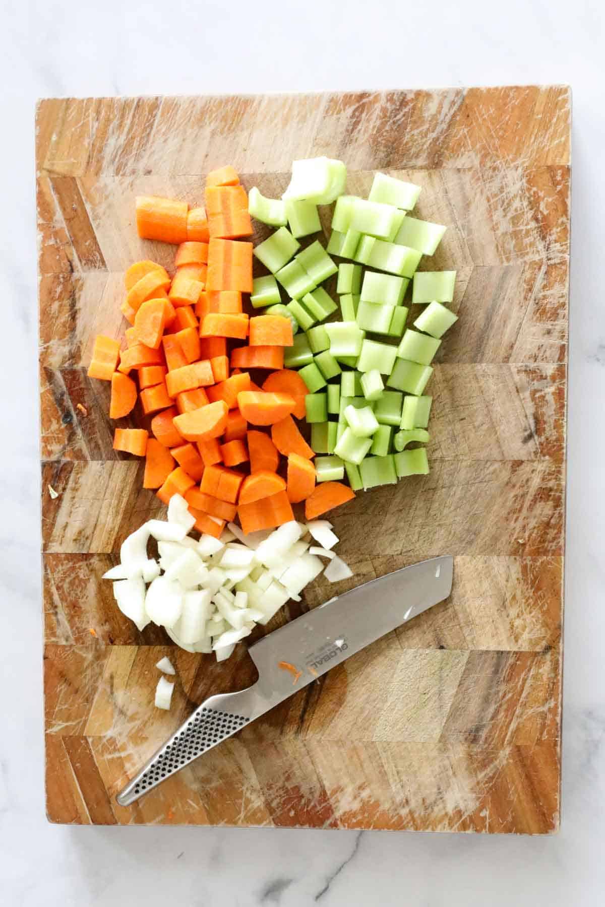Chopped carrots, celery and onion on a wooden chopping board.