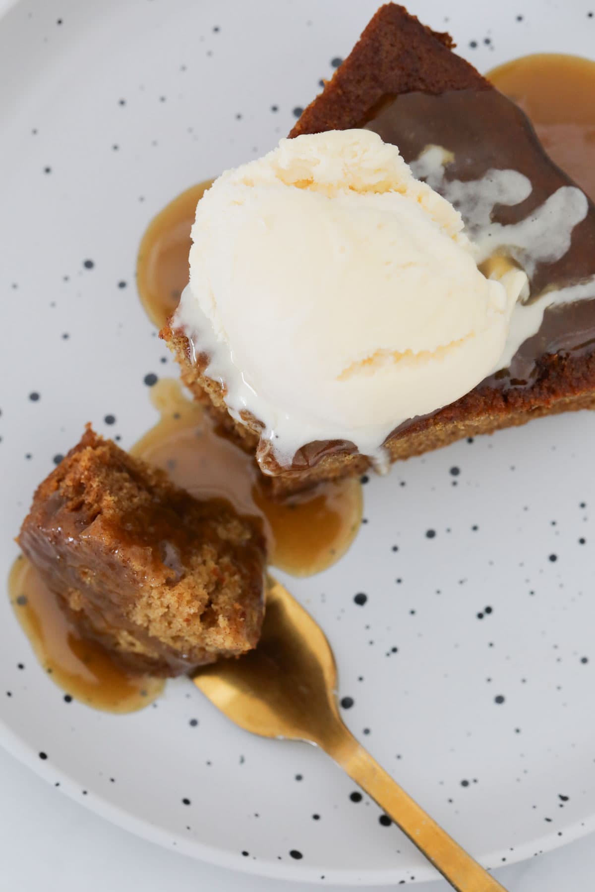Overhead shot of a wedge of sticky date pudding and ice cream, with some on a spoon.