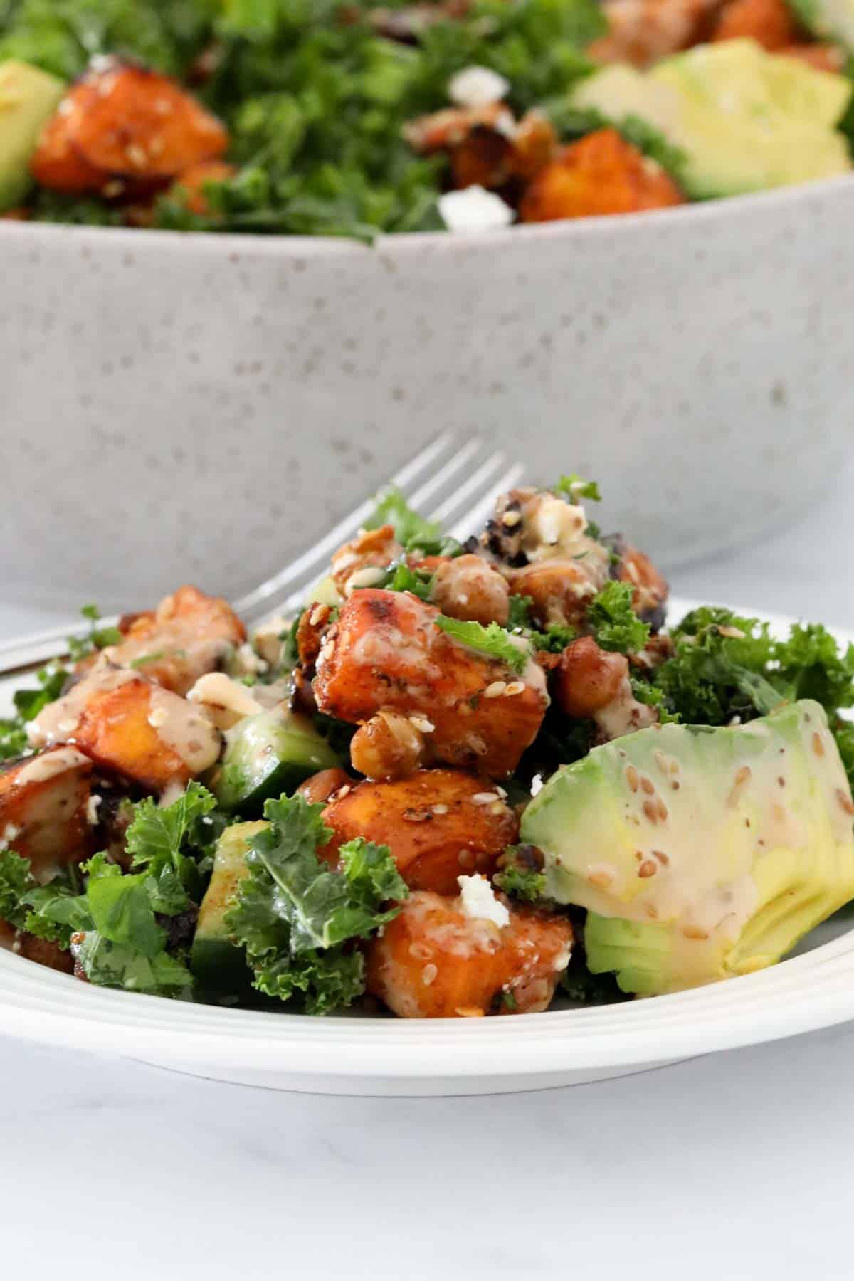 A plate of sweet potato and kale salad, with a serving bowl of salad just visible behind.