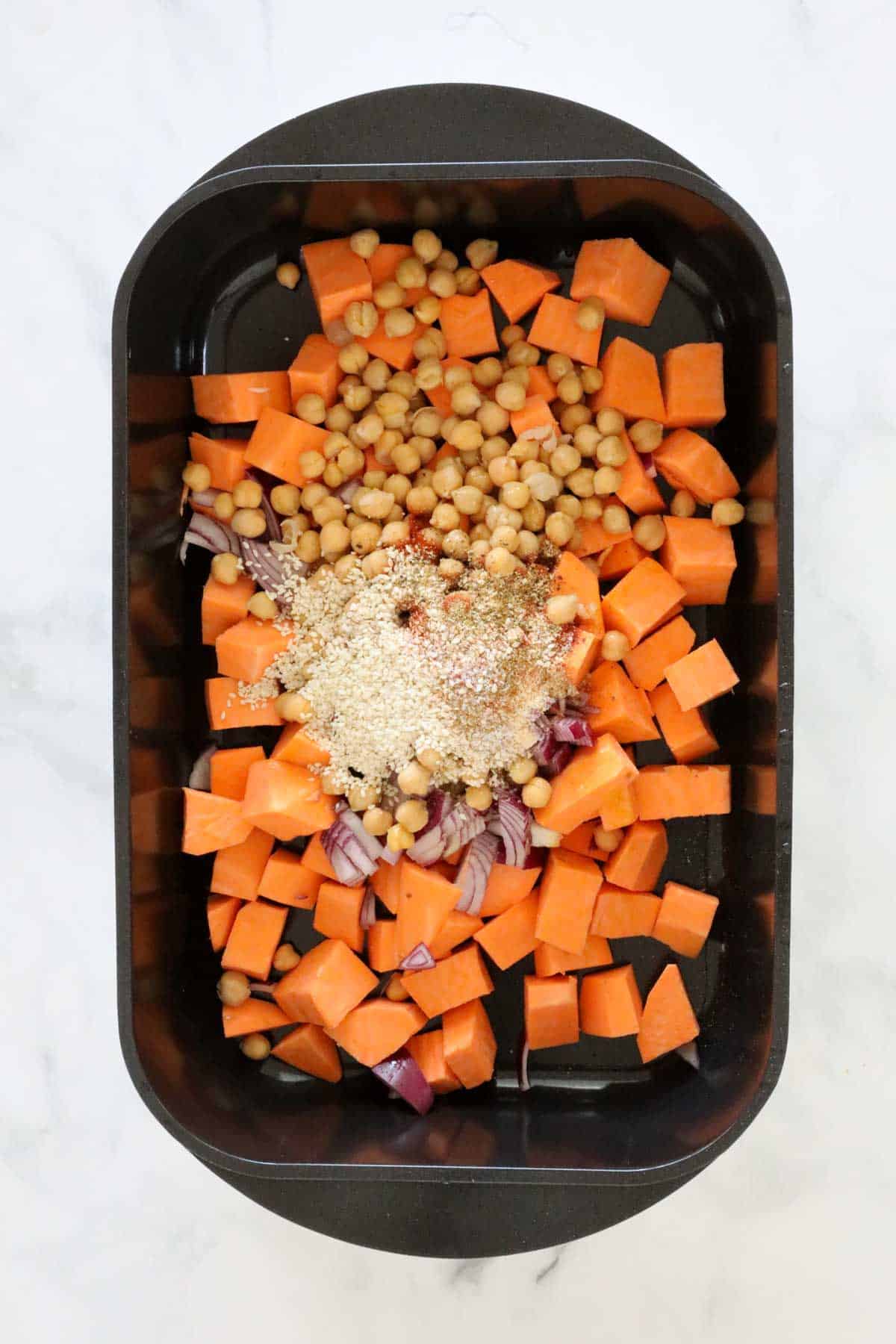 Sweet potato cubes, chickpeas, red onion and dried spices on a baking tray.