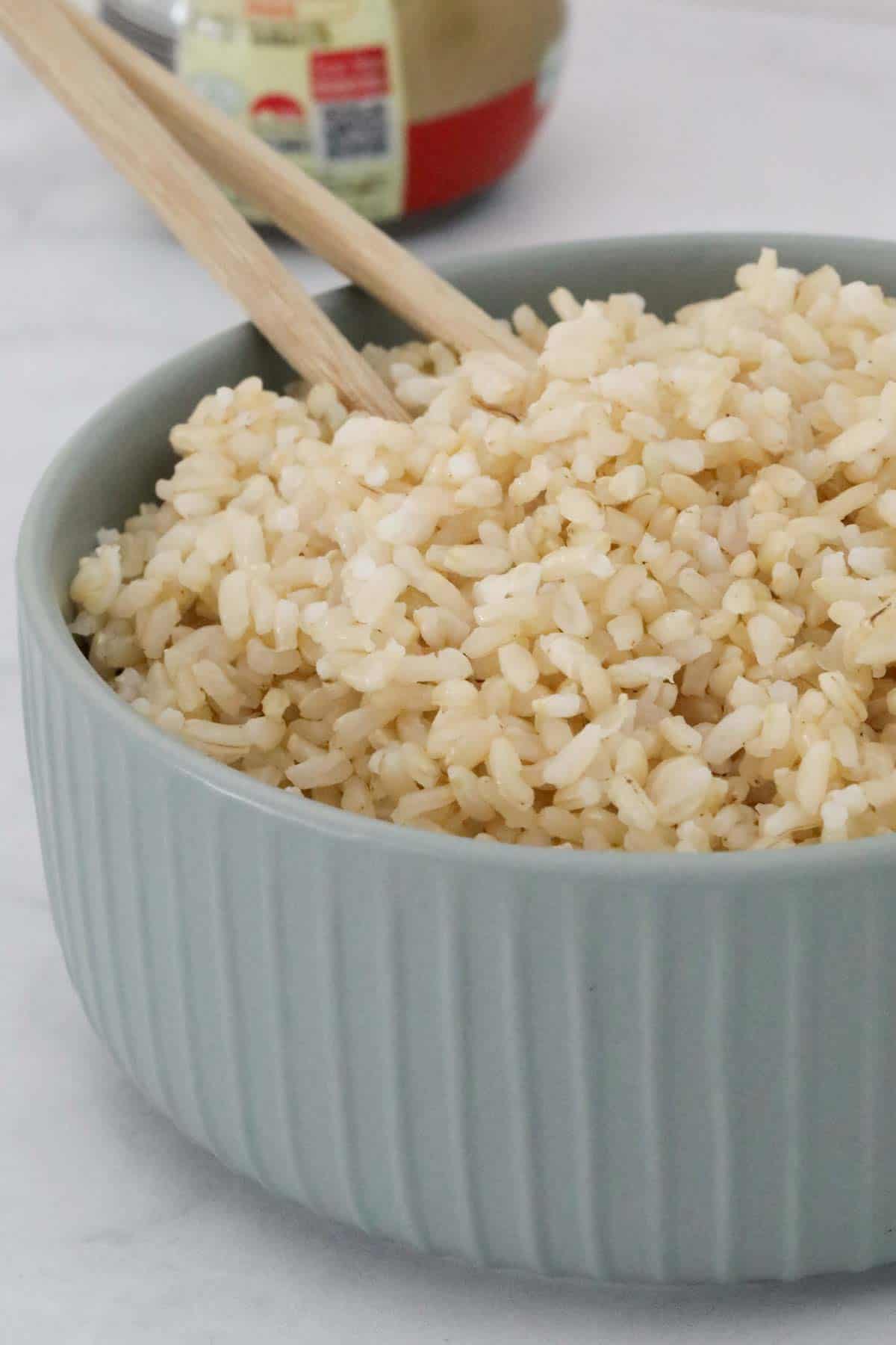 Chopsticks in a bowl of fluffy brown rice.