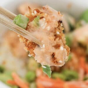 Chopsticks holding a piece of panko crumbed chicken with bang bang creamy sauce.