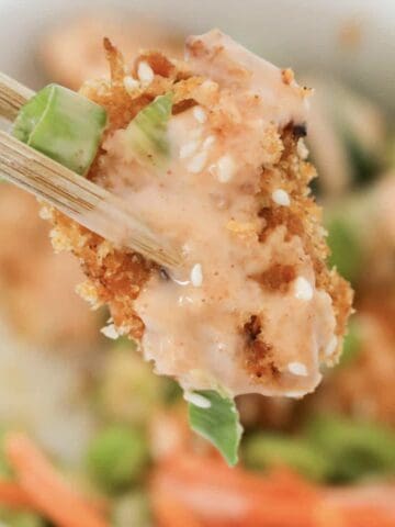 Chopsticks holding a piece of panko crumbed chicken with bang bang creamy sauce.