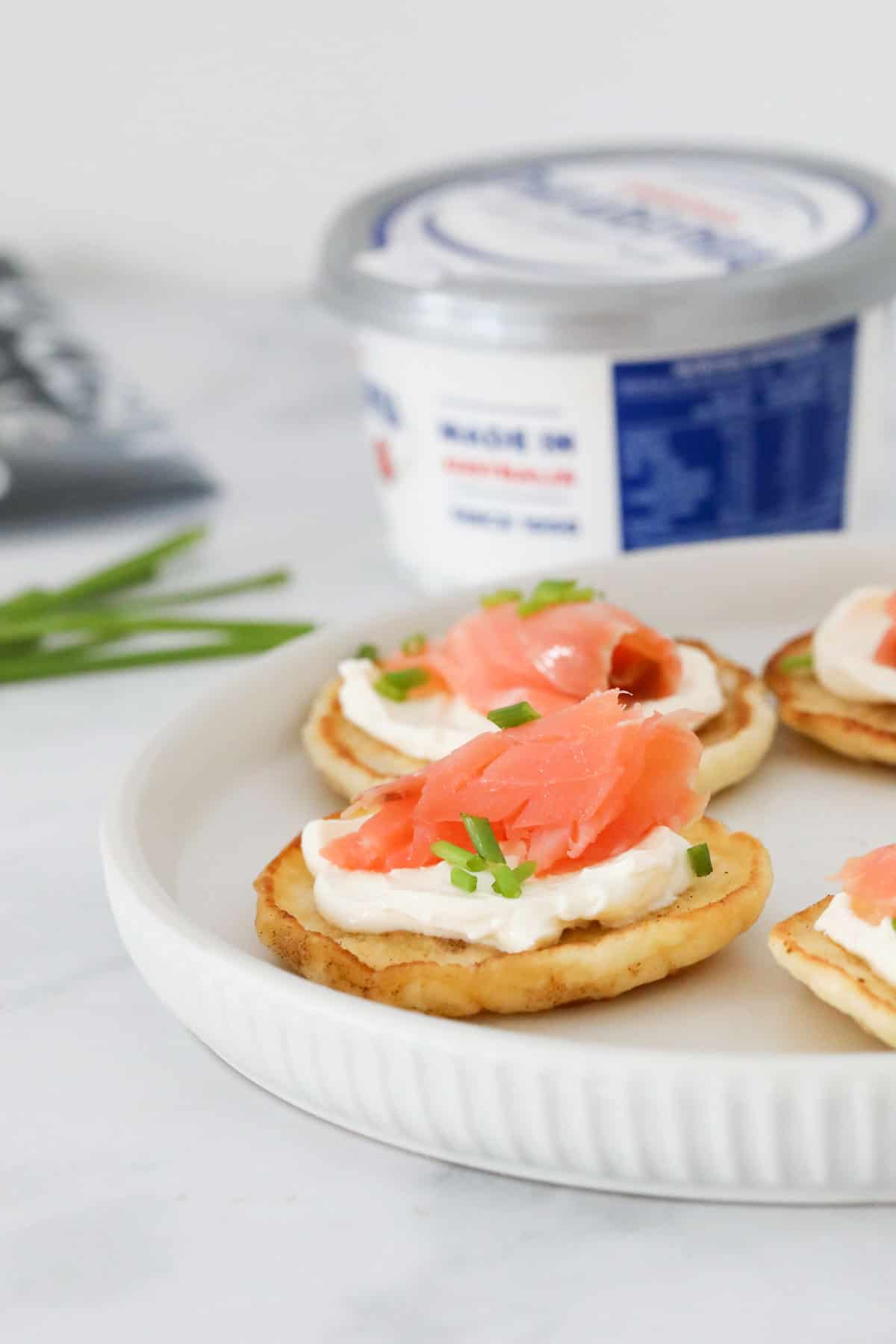 Blinis with smoked salmon served as appetisers on a white platter.