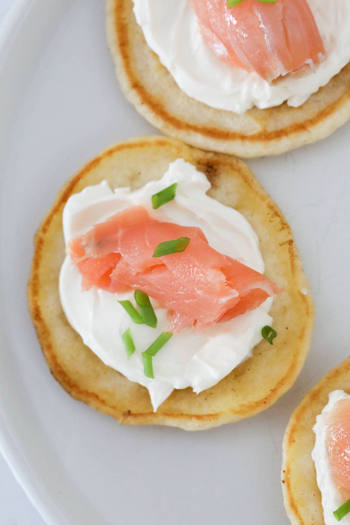 An overhead shot of a mini pancake, garnished with cream cheese and a small piece of salmon.