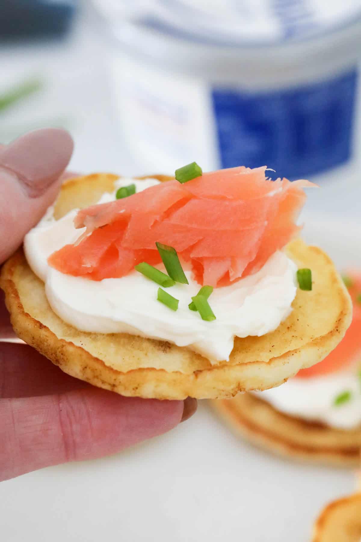 A hand holding a blini topped with cream cheese and smoked salmon.