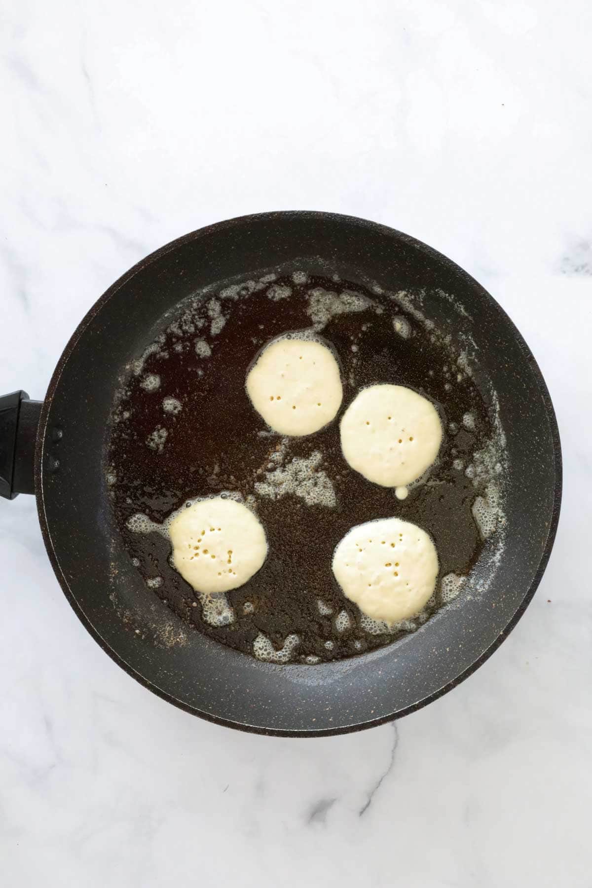 Four blinis being fried in butter in a frying pan.