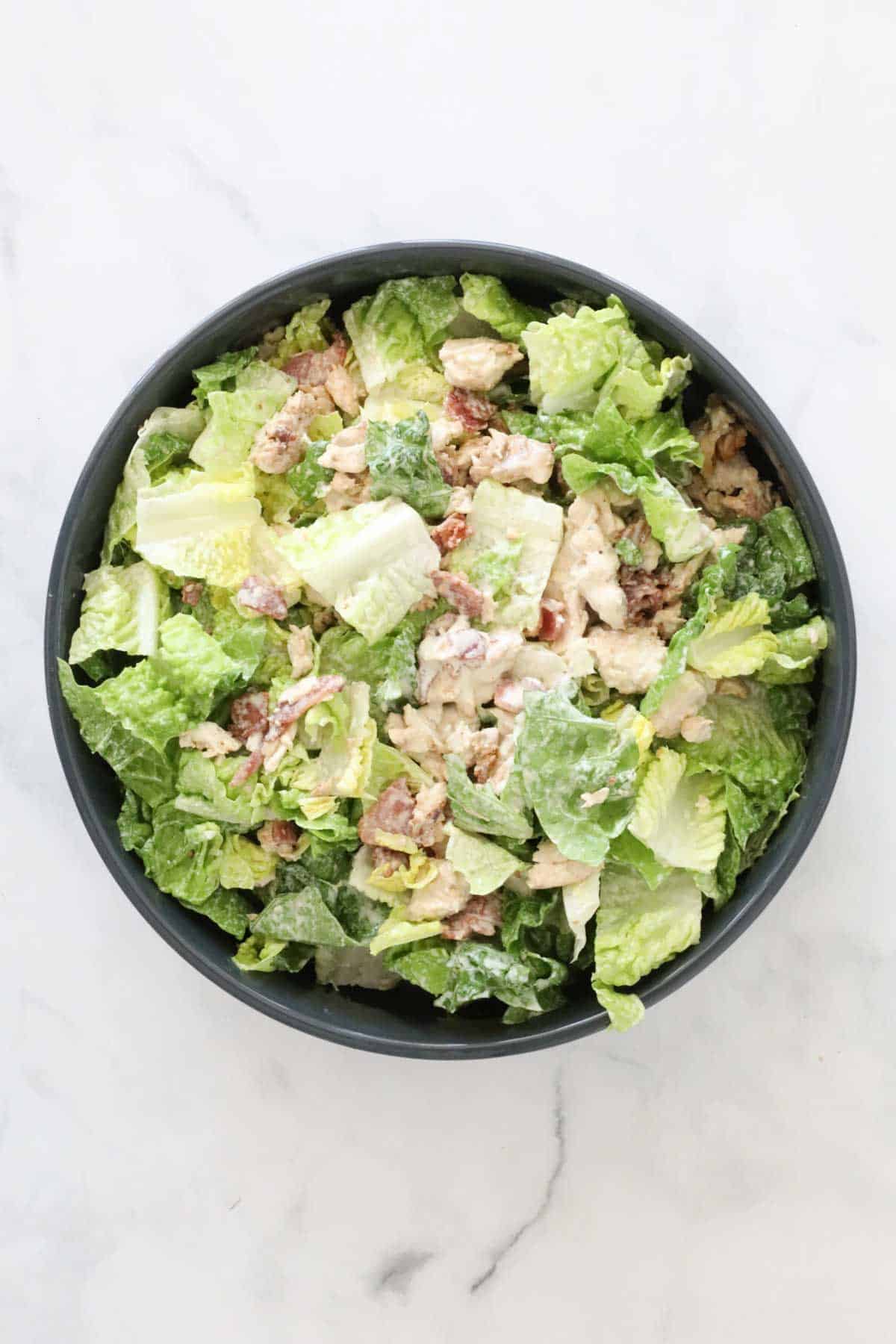 The dressing coated bacon, chicken and lettuce in a serving bowl.