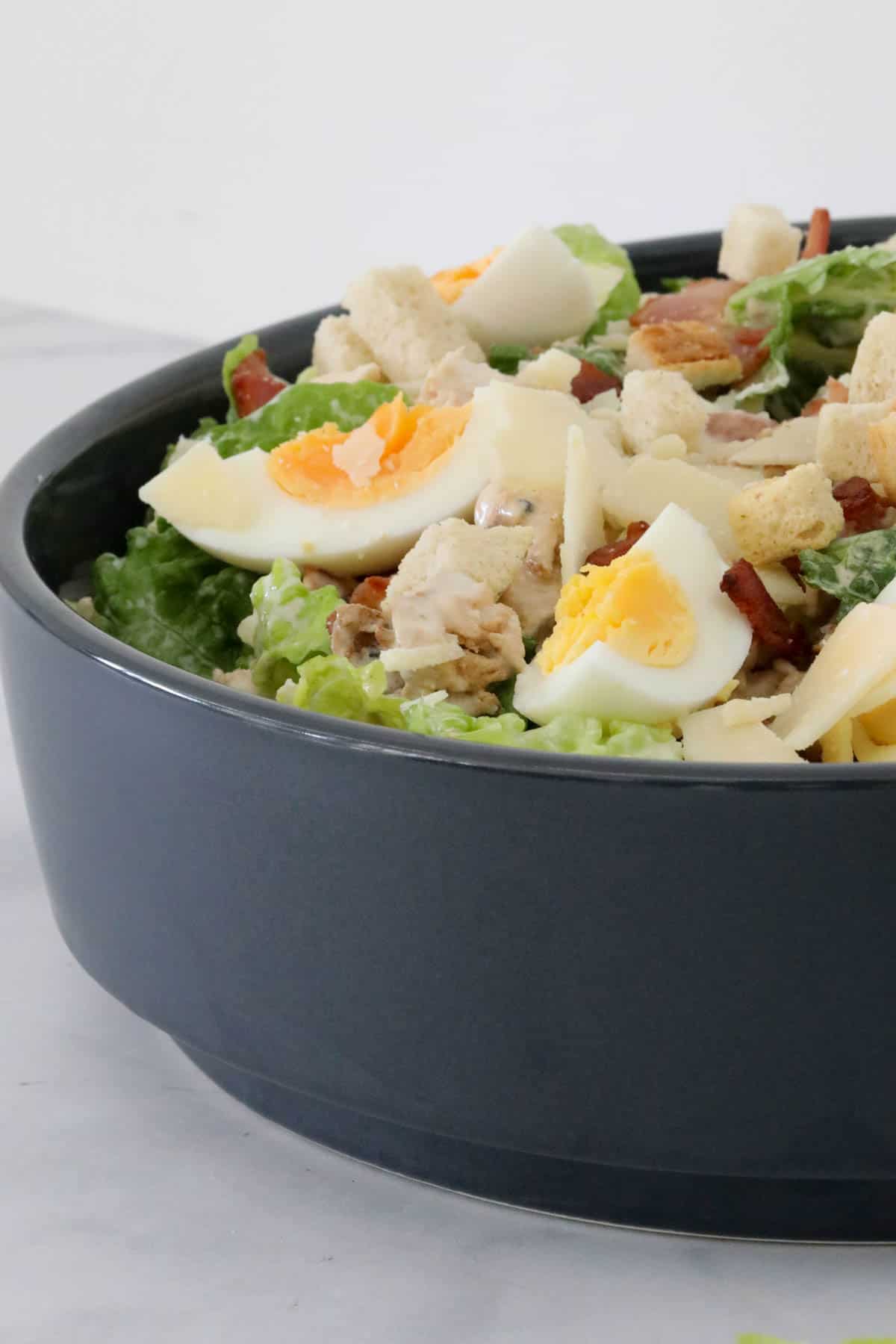 A black bowl filled with chicken Caesar salad.