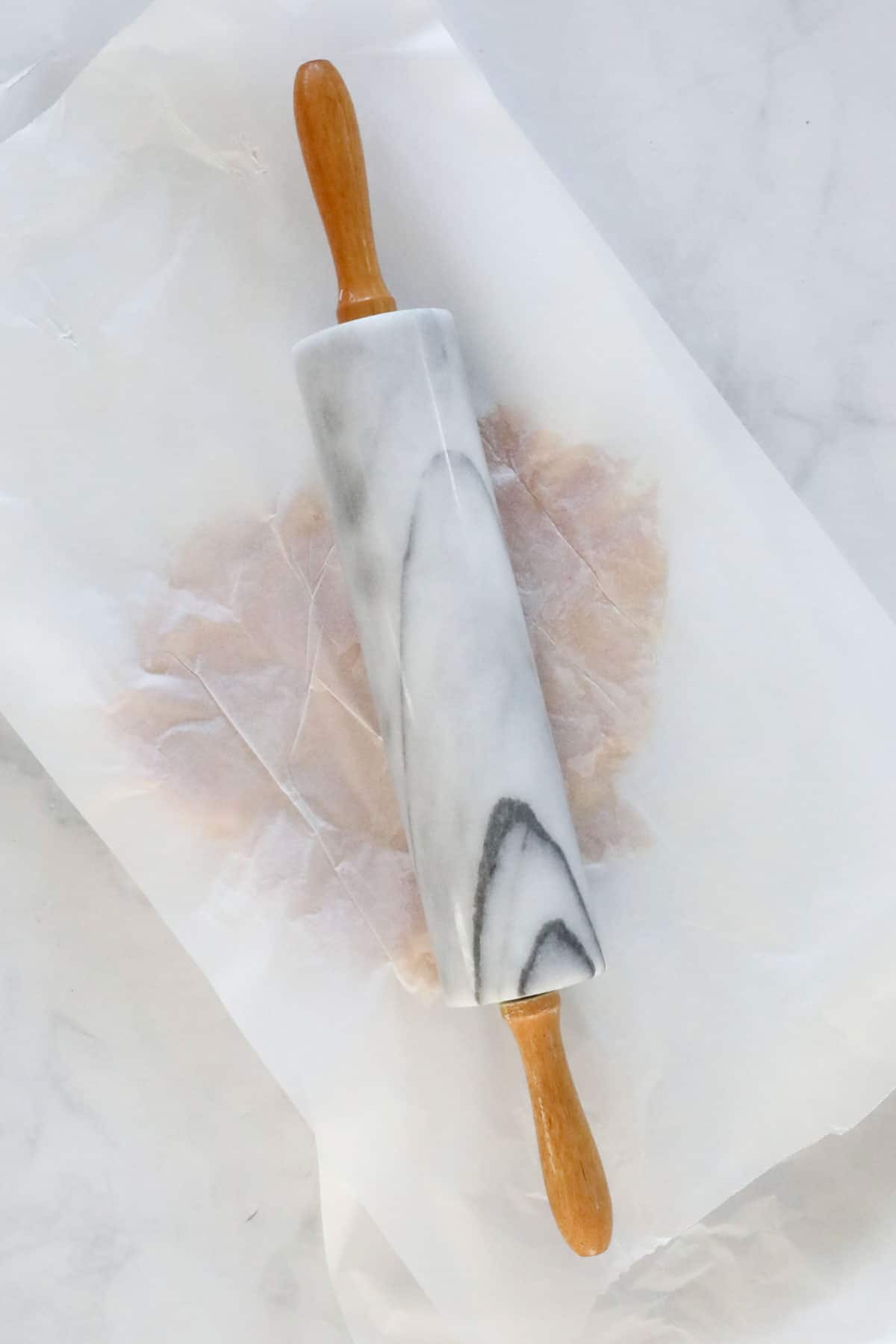 The chicken breasts between two sheets of baking paper being flattened with a rolling pin.