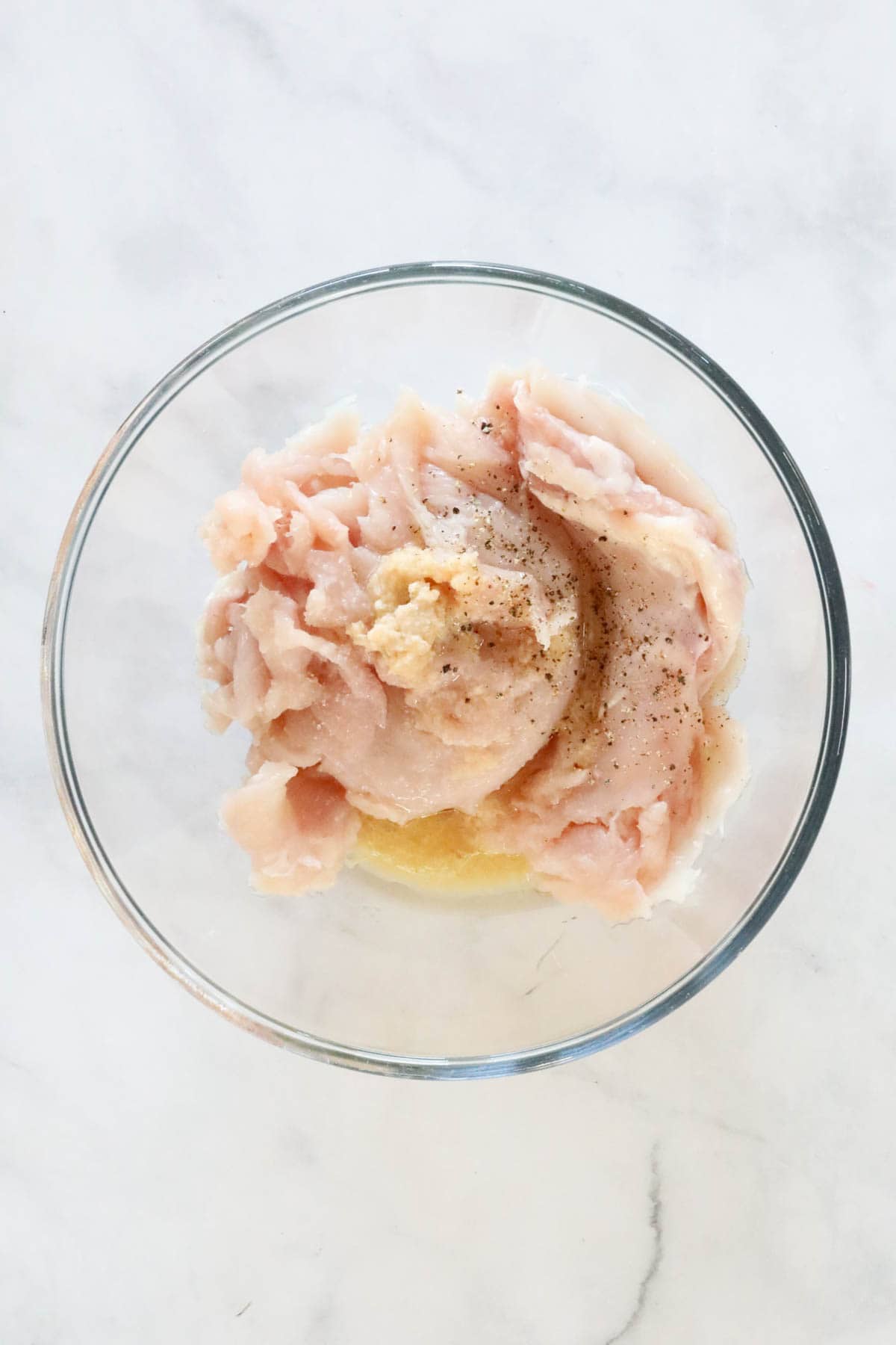 The thin chicken pieces in a bowl with the olive oil, garlic, salt and pepper.