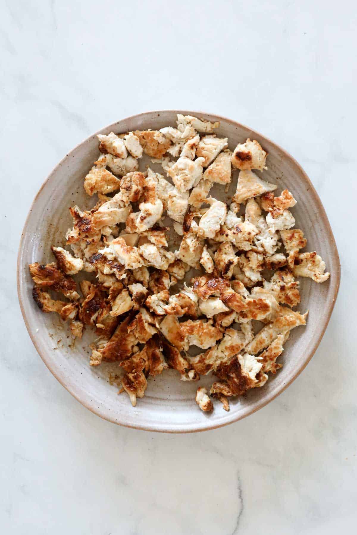 Cooked chicken breasts on a plate, chopped in to bite size pieces.