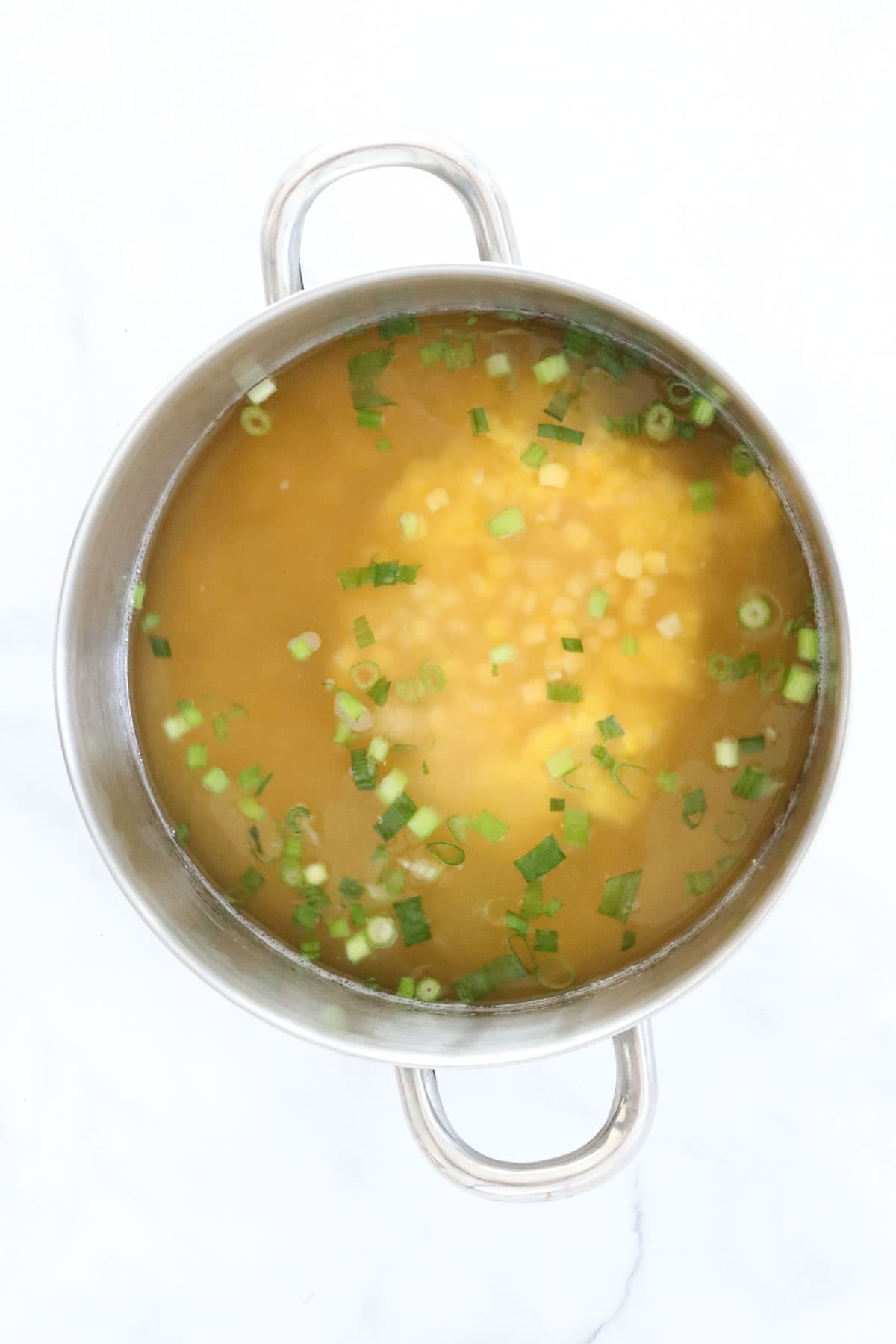 Chicken stock, corn kernels and spring onions in a pot of corn soup.