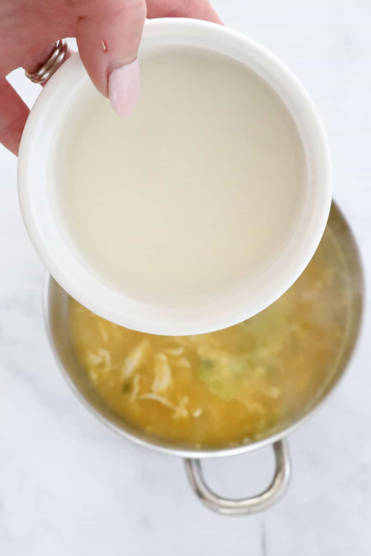 Dissolved cornflour being poured into a pot of soup.