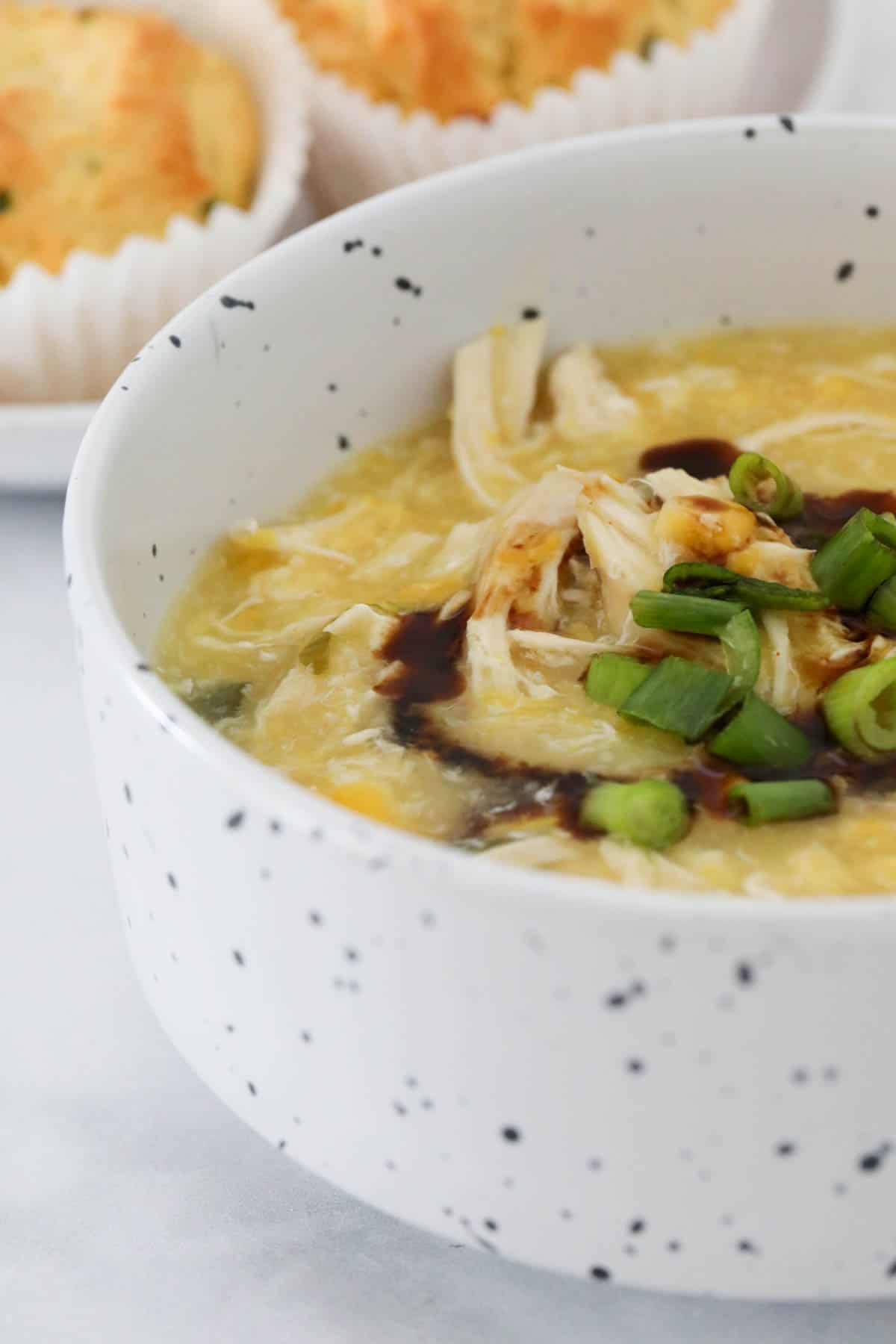 A bowl of corn soup topped with chicken, spring onions and soy sauce.