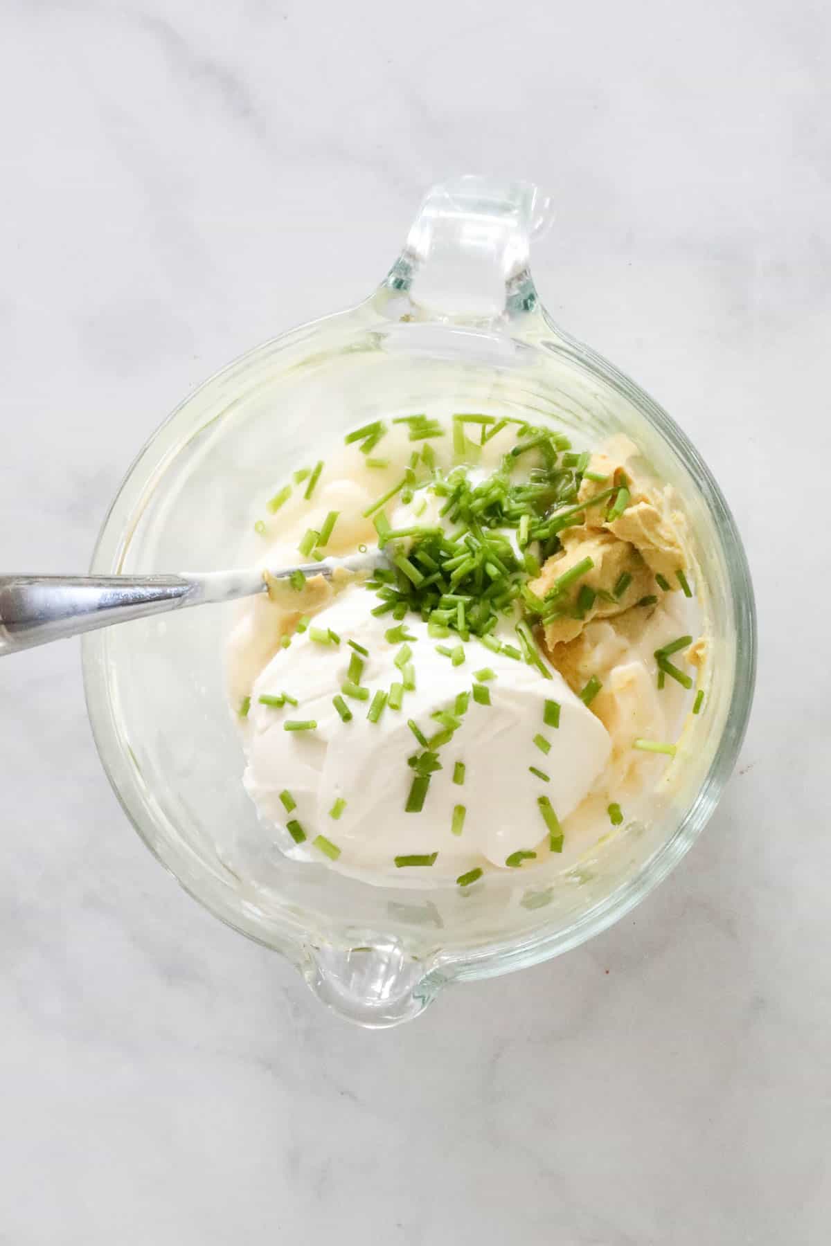 The mayonnaise, sour cream, mustard, vinegar, sugar and chopped chives in a small jug.