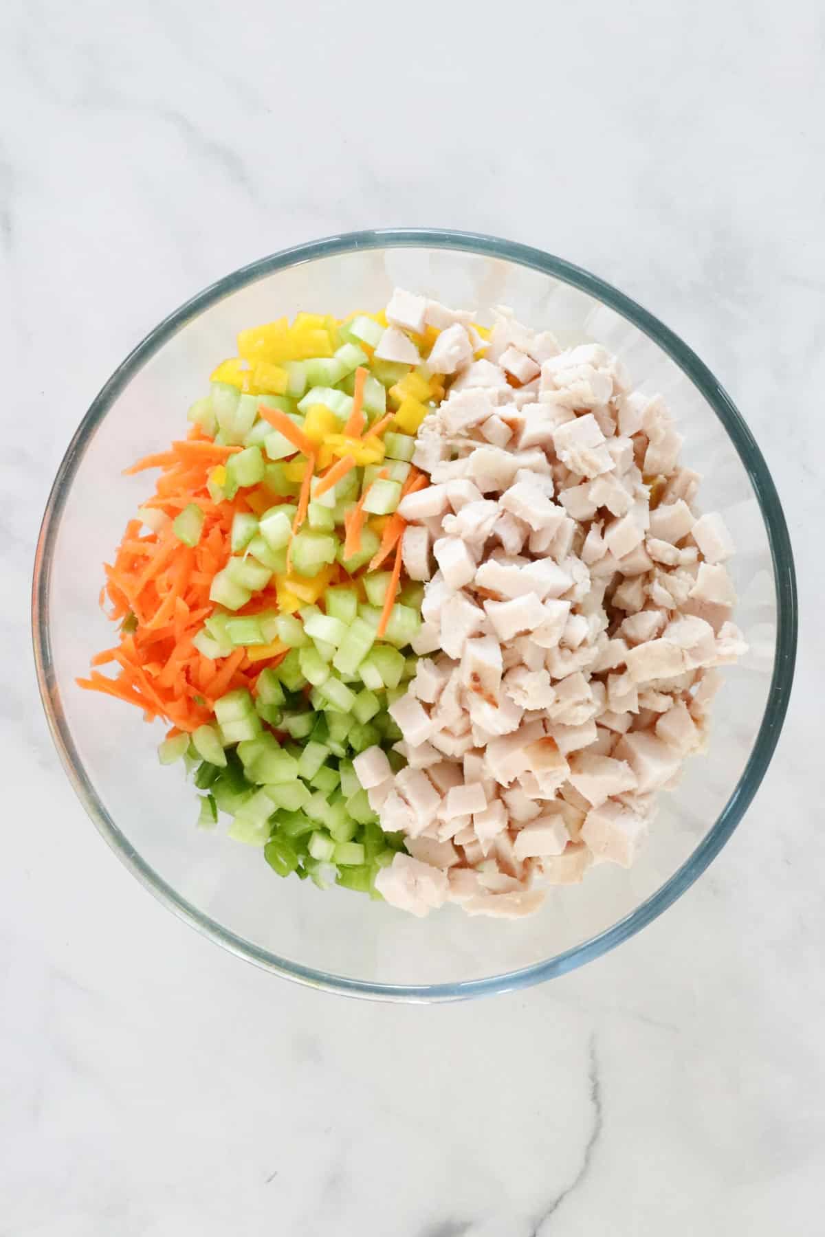 Chopped chicken, cucumber, celery, carrot and capsicum added to a bowl with the cooked pasta.