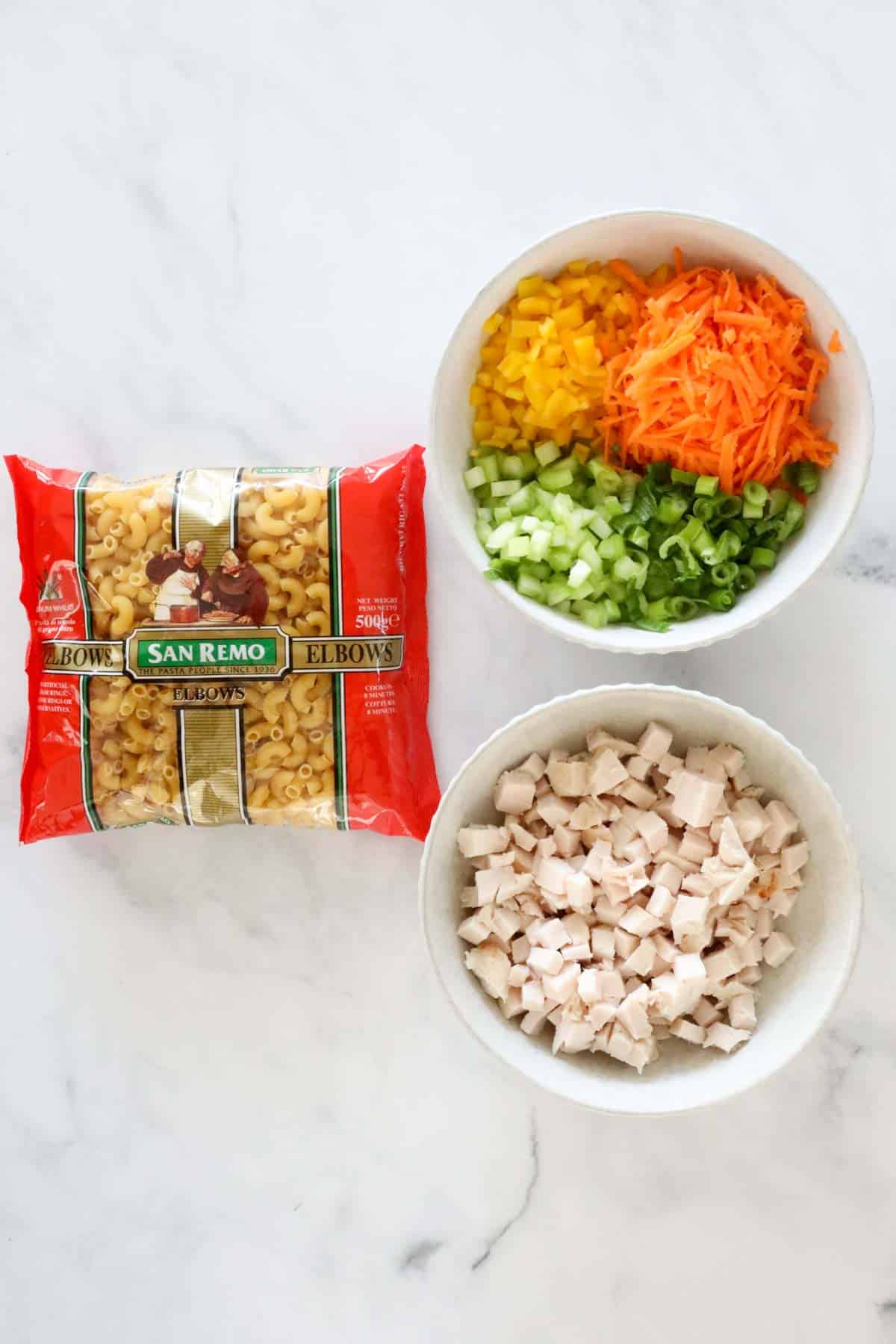 Chicken pasta salad ingredients placed in bowls, together with a packet of macaroni.