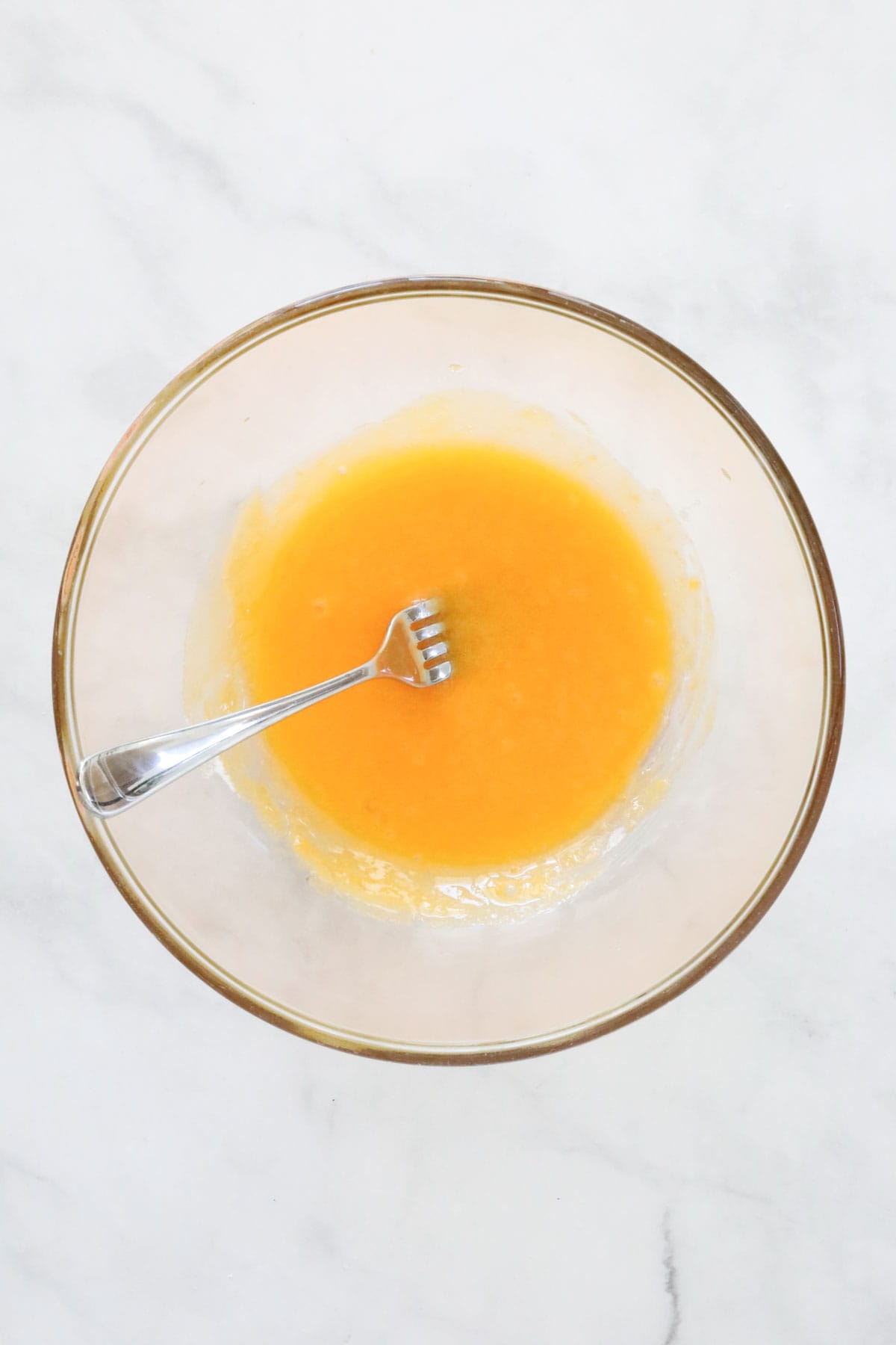 The whisked egg yolks and caster sugar in a clear bowl with a fork.