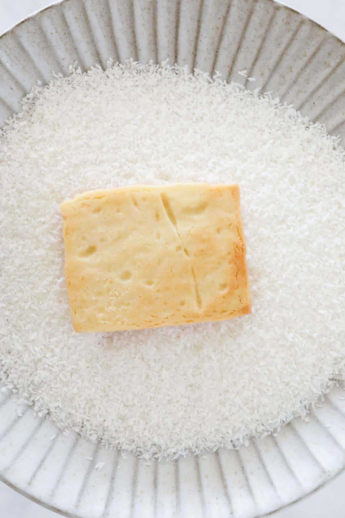 The cookie on a plate of desiccated coconut, with the marshmallow icing side face down.