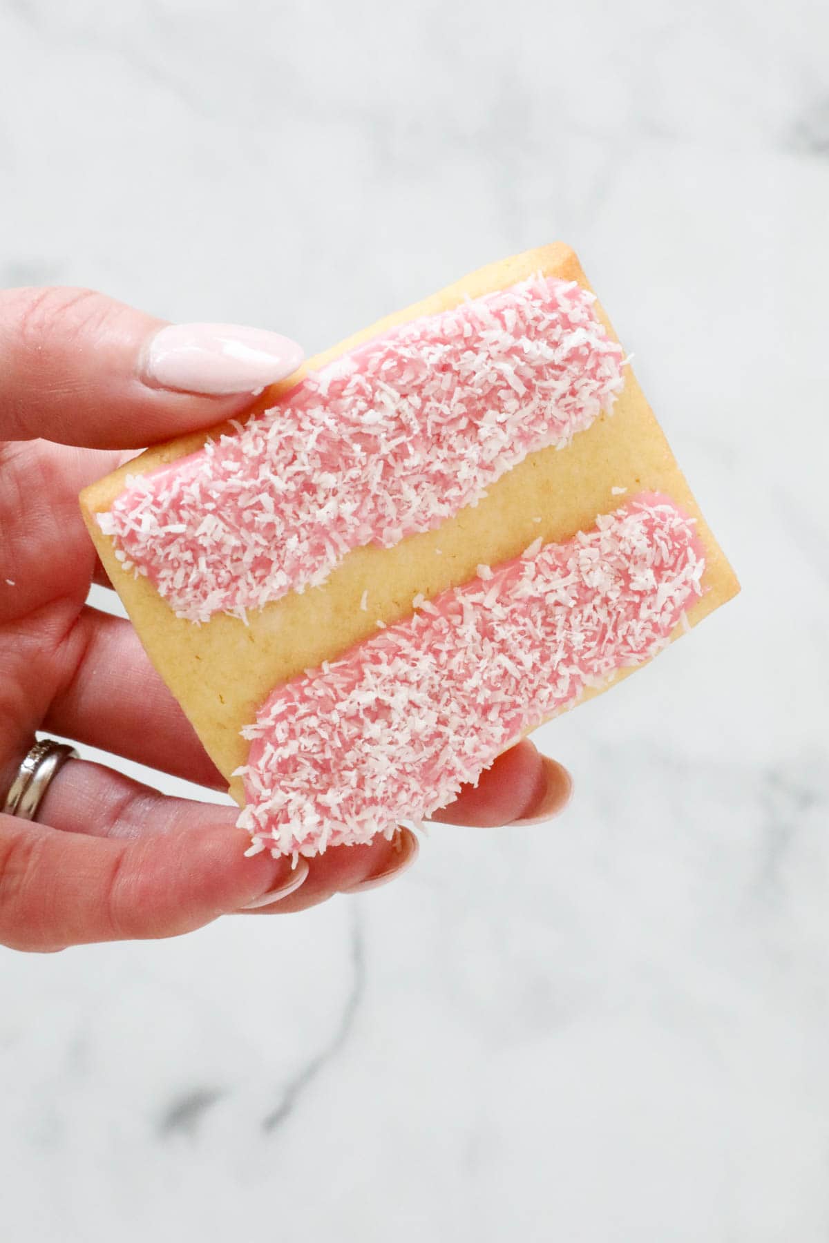 A hand holding the coconut decorated iced vovo biscuit.