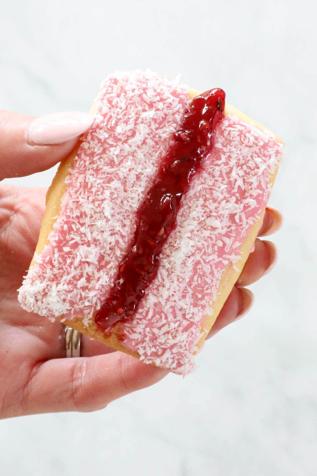 A hand holding the iced vovo biscuit with jam spread down the centre.