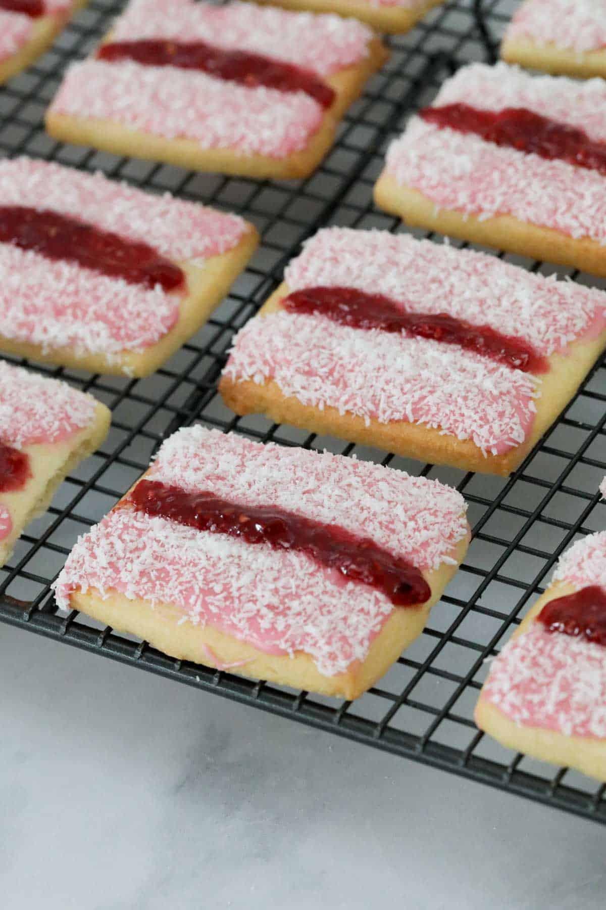 A number of pink iced cookies  on a wire cooling rack.