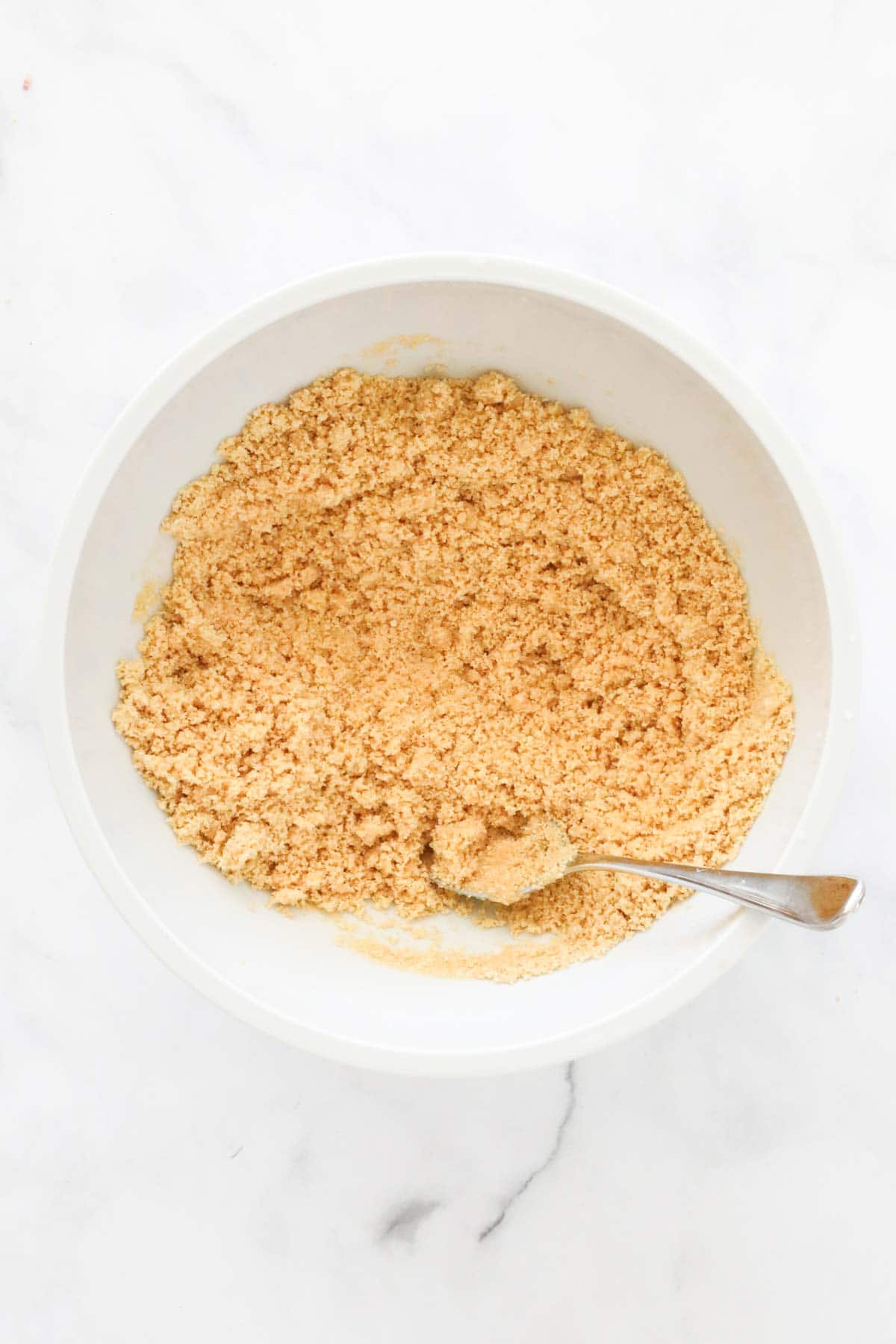 The crushed biscuits in a bowl being mixed with melted butter.