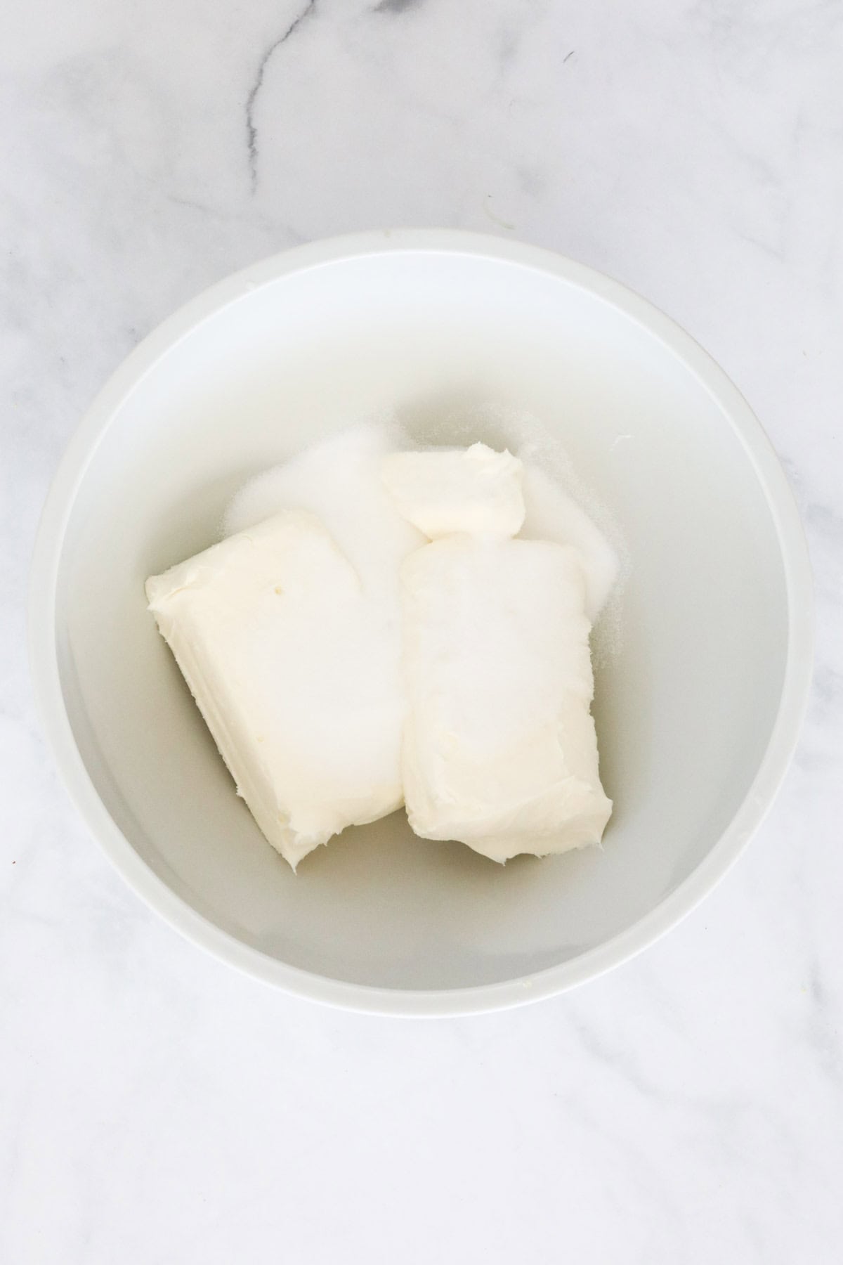 Blocks of cream cheese placed in a bowl with sugar.