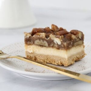 A piece of vanilla cheesecake topped with a caramel pecan layer.