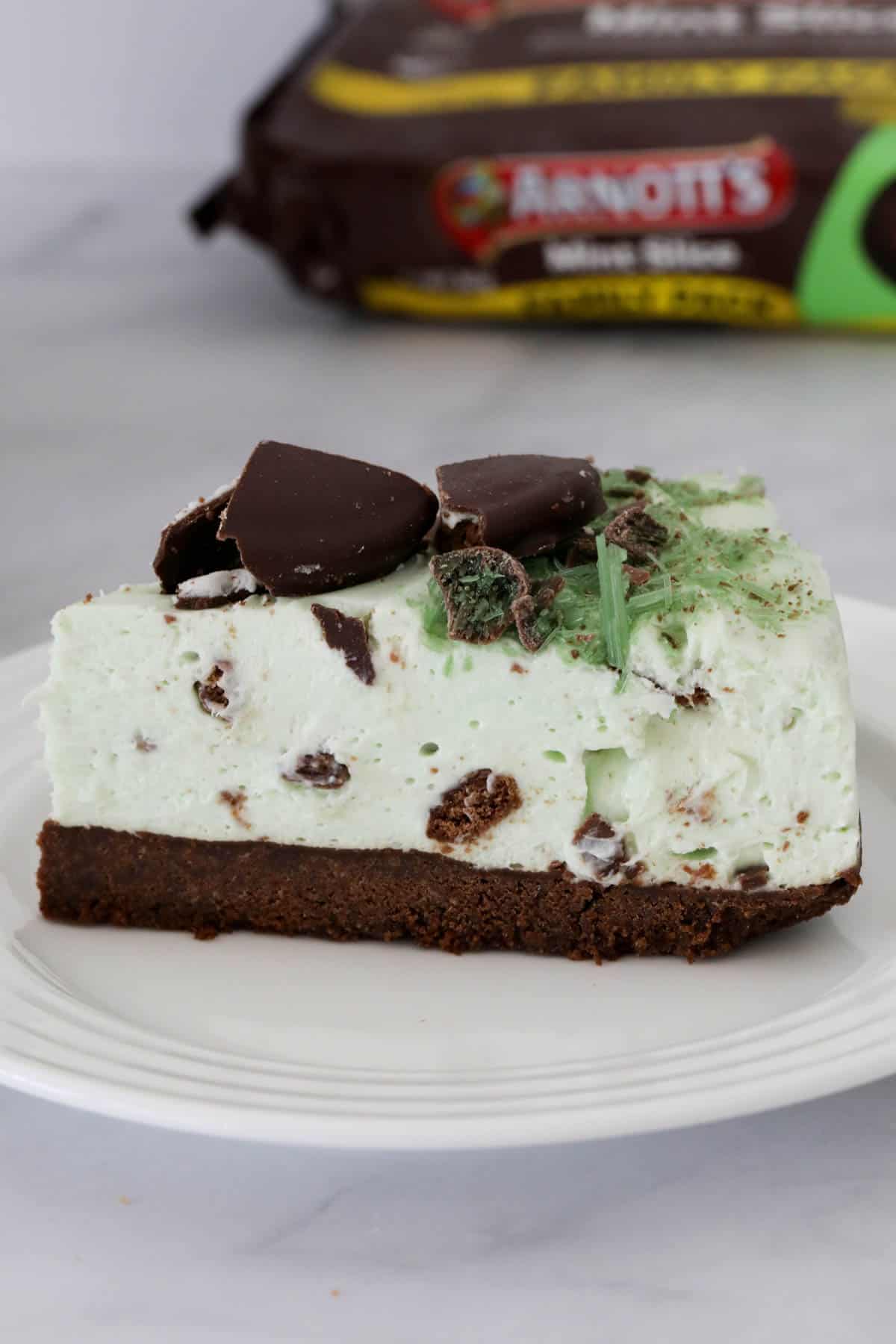 Side view of a slice of peppermint cheesecake, with a packet of Arnott's Mint Slice biscuits just visible behind.