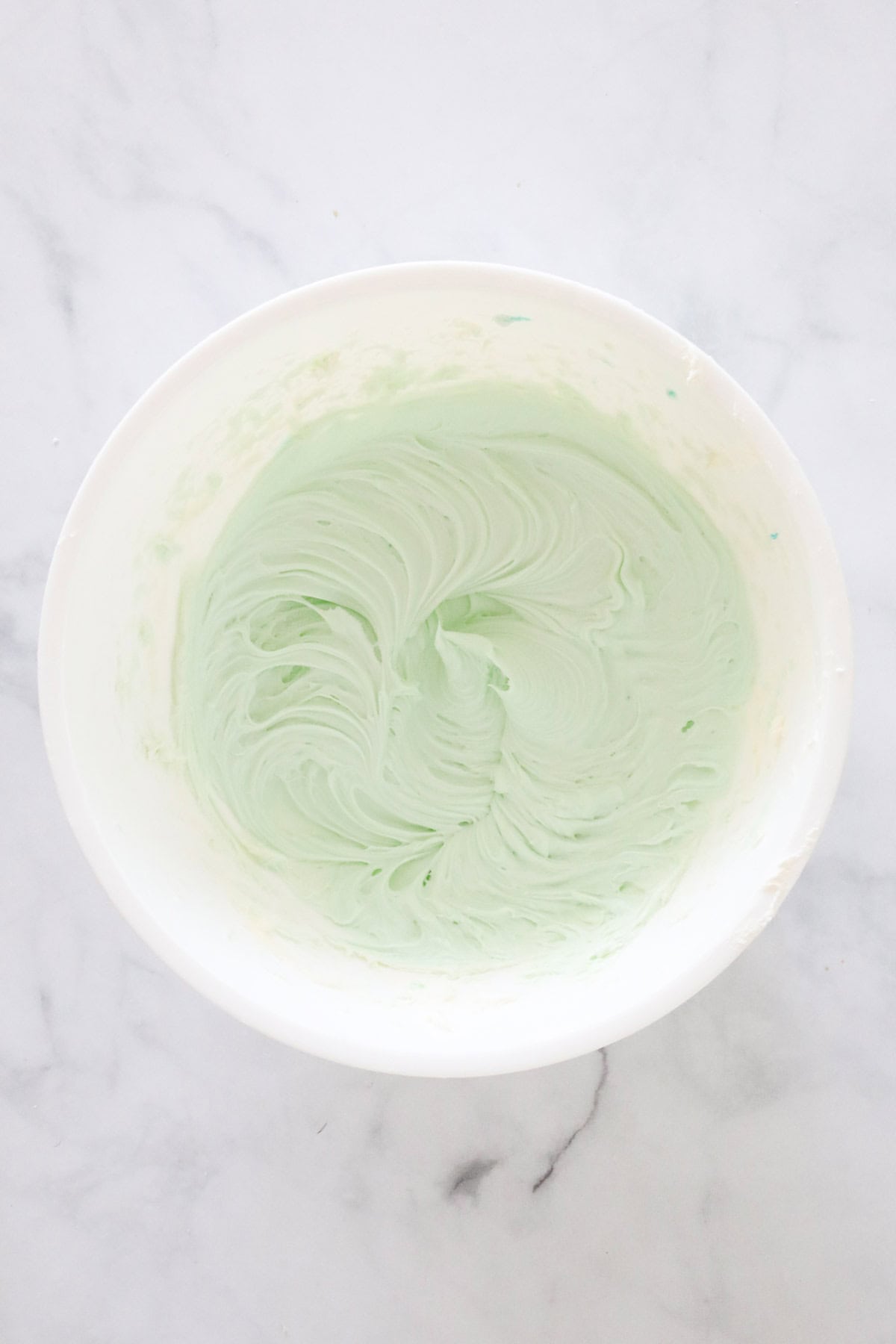 Cream cheese whipped with green food colouring in a white bowl.